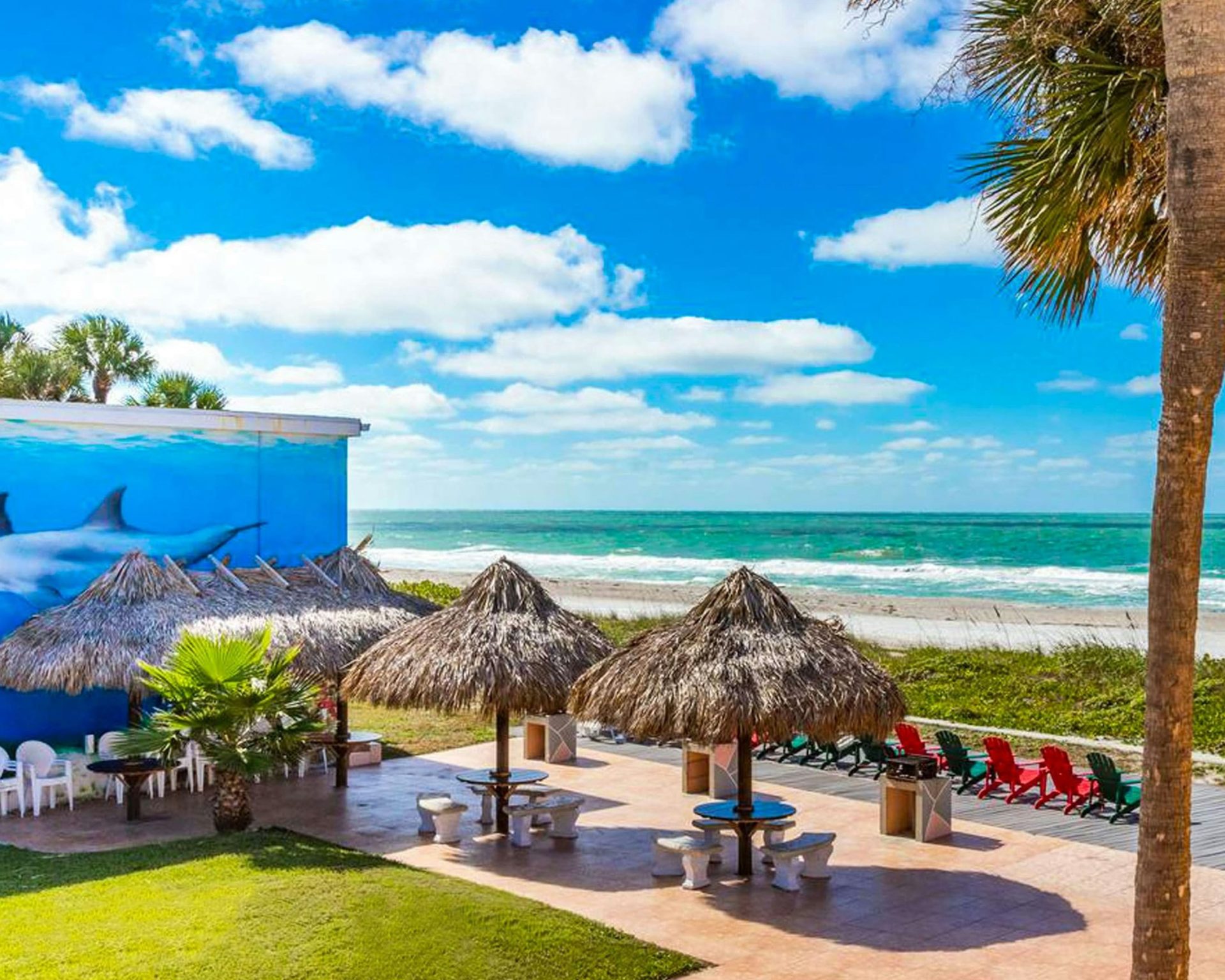 Oceanfront patio at Belleair Beach hotel with tiki huts, picnic tables, and beach chairs overlooking the Gulf of Mexico.