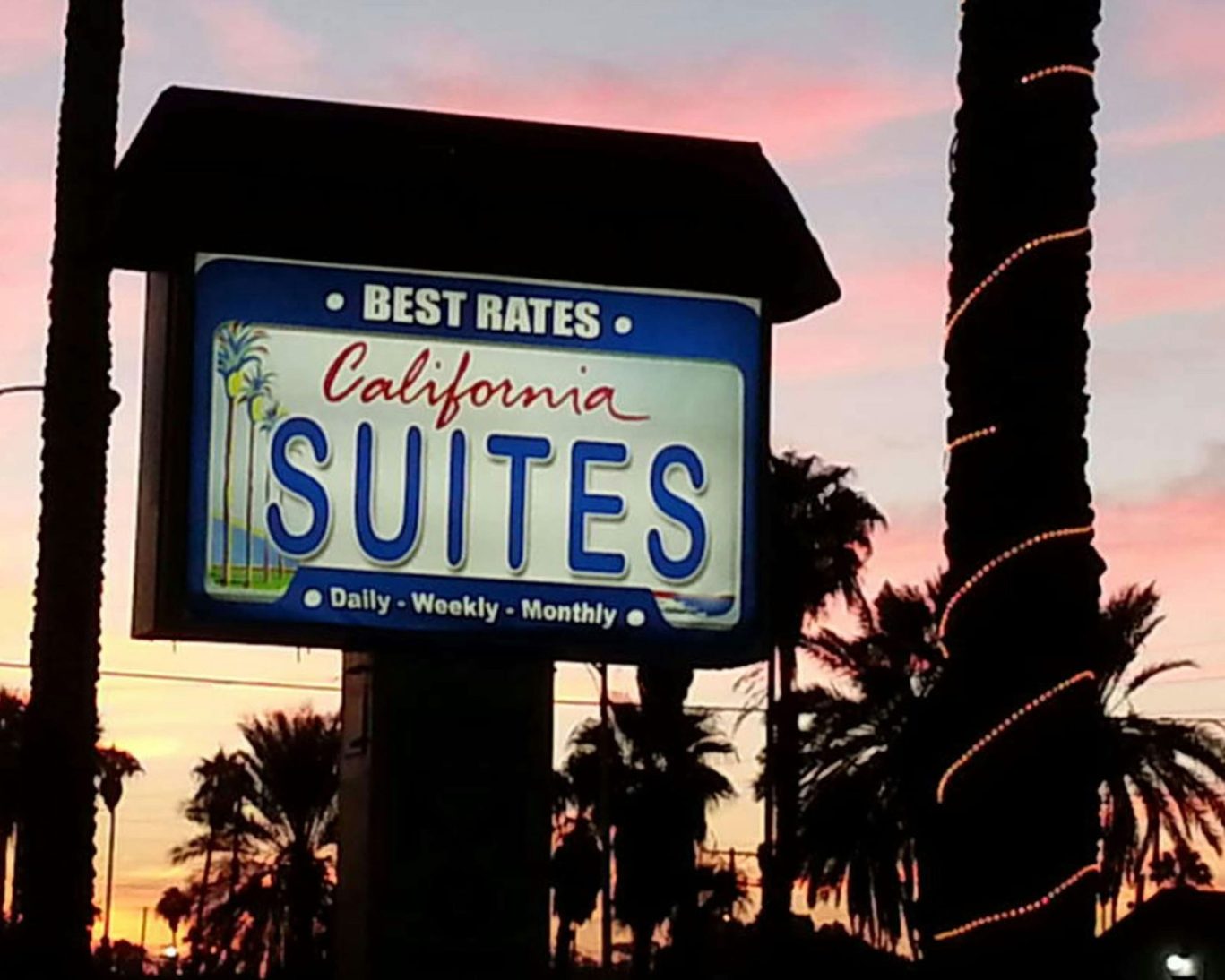 Illuminated California Suites Motel sign at sunset with palm trees in the background.
