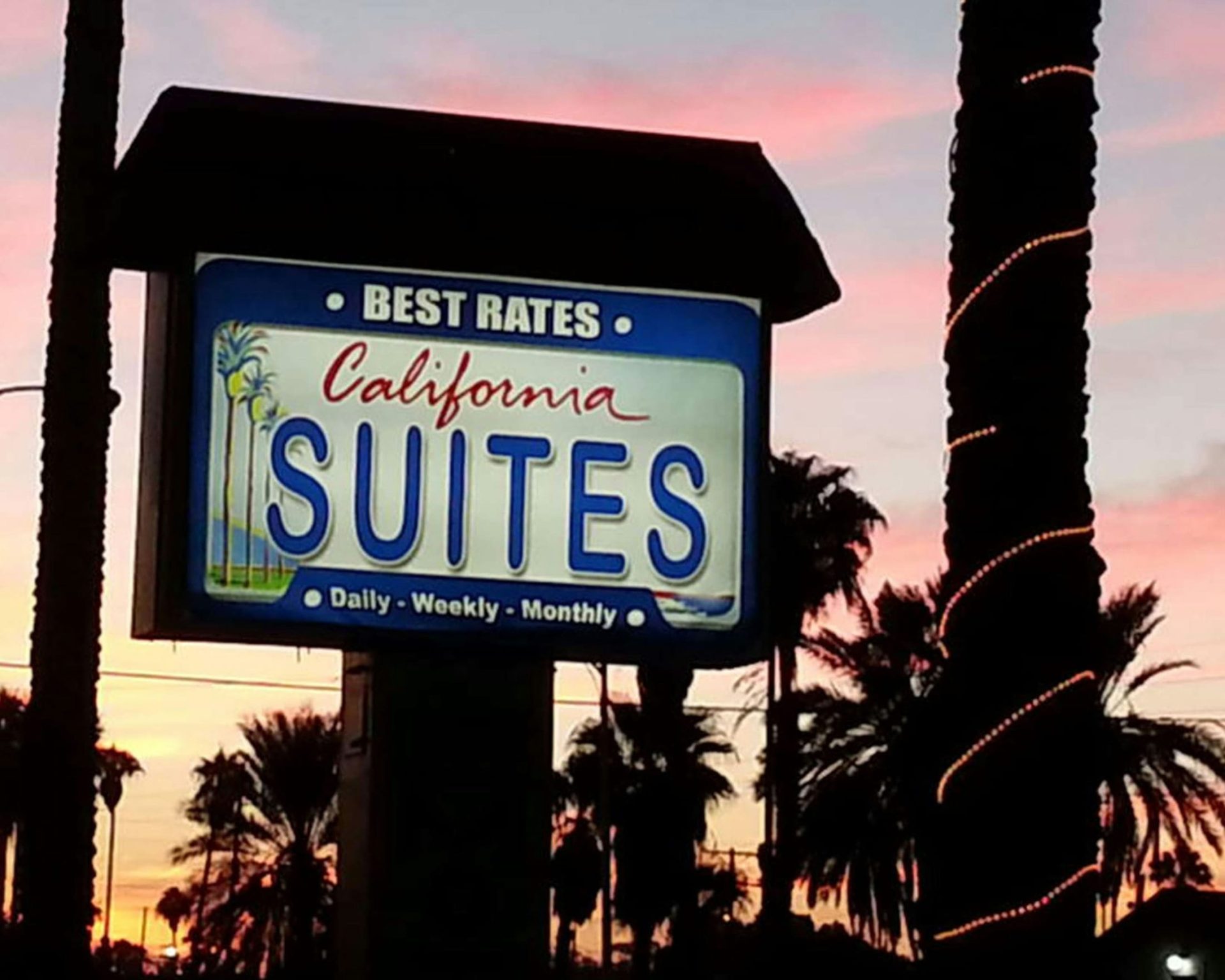 Illuminated California Suites Motel sign at sunset with palm trees in the background.