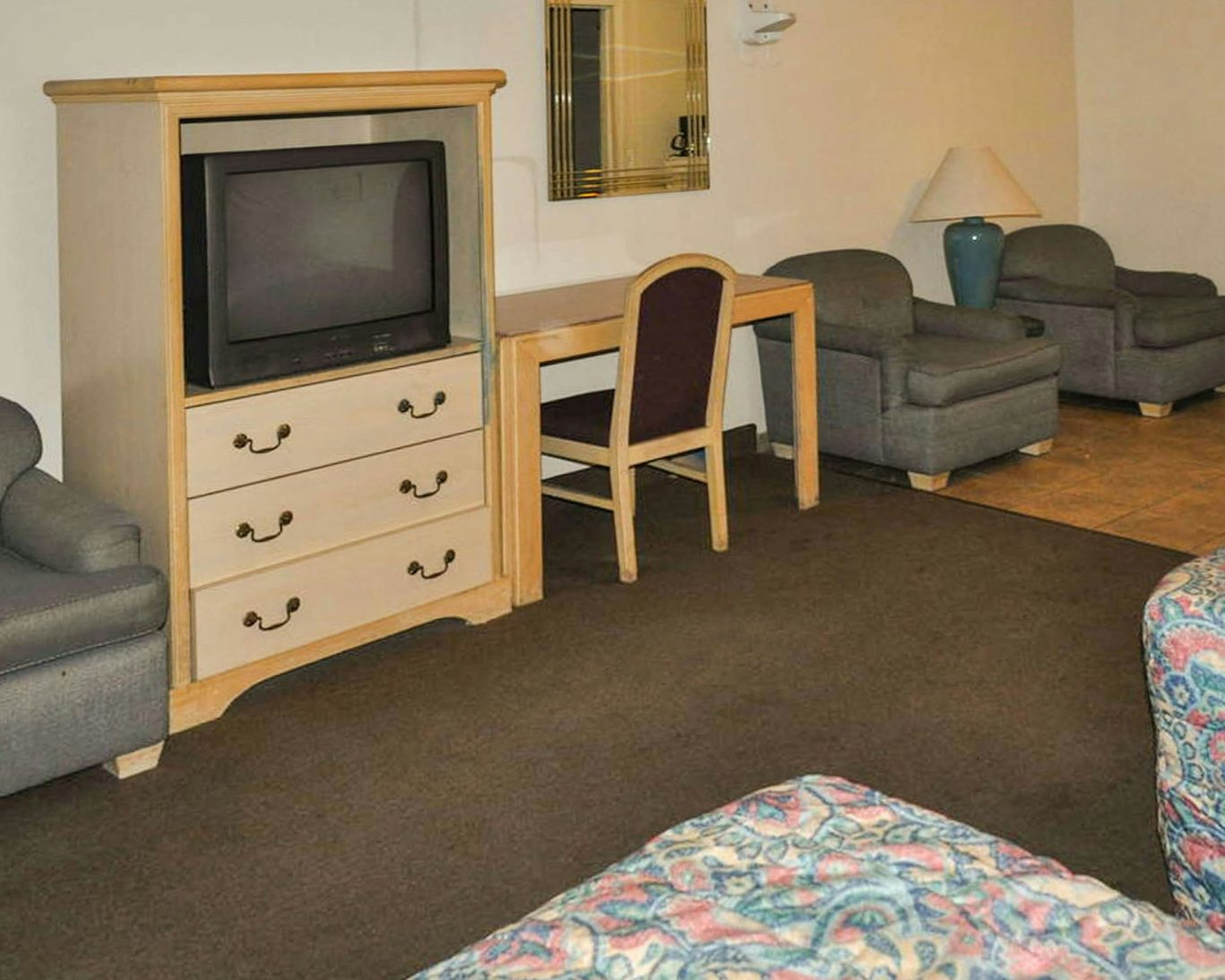 Interior of a California Suites Motel room featuring armchairs, desk, TV cabinet, and carpeted floor.