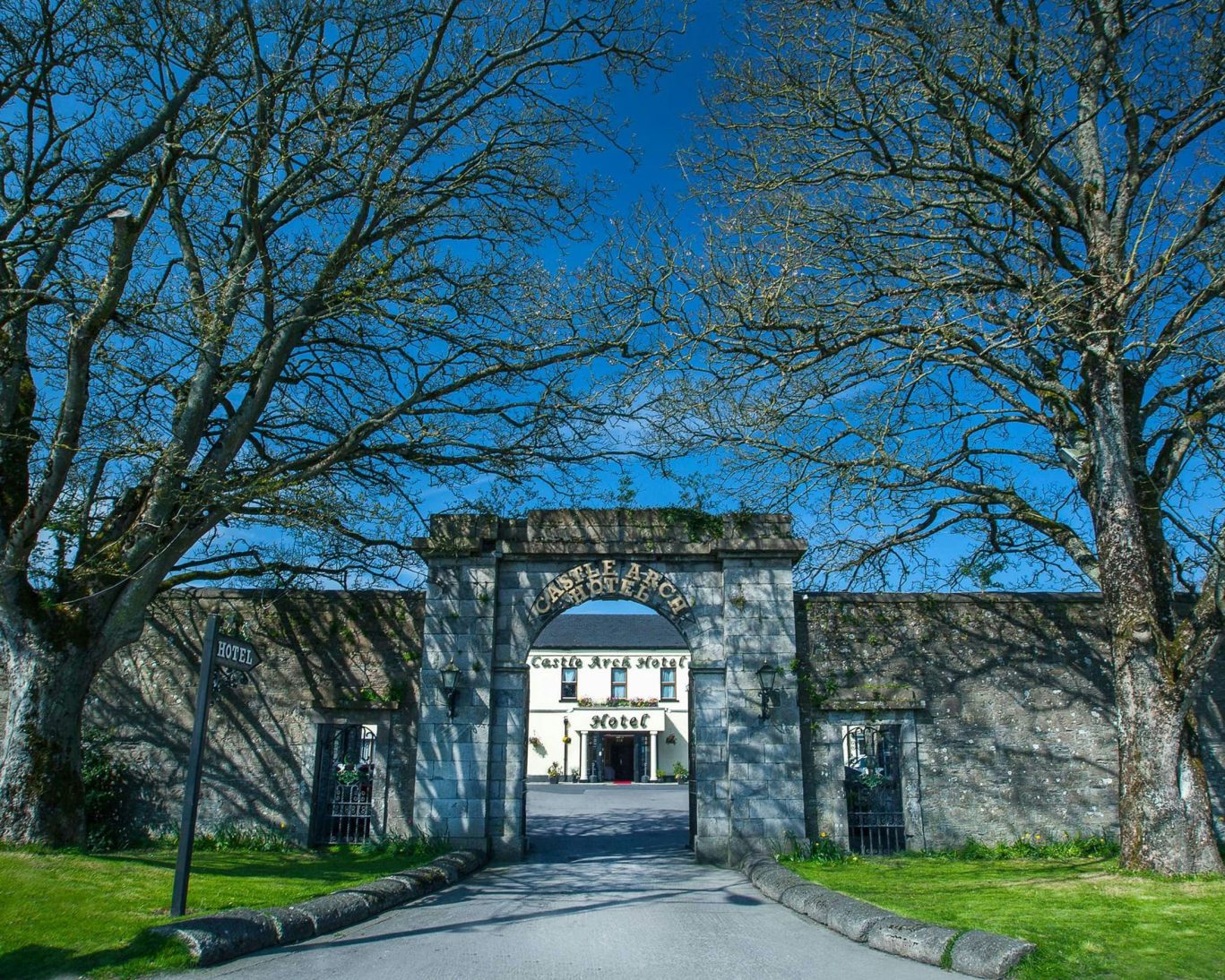 Historic stone arch entrance to The Castle Arch Hotel in Trim, Ireland with tree-lined drive.