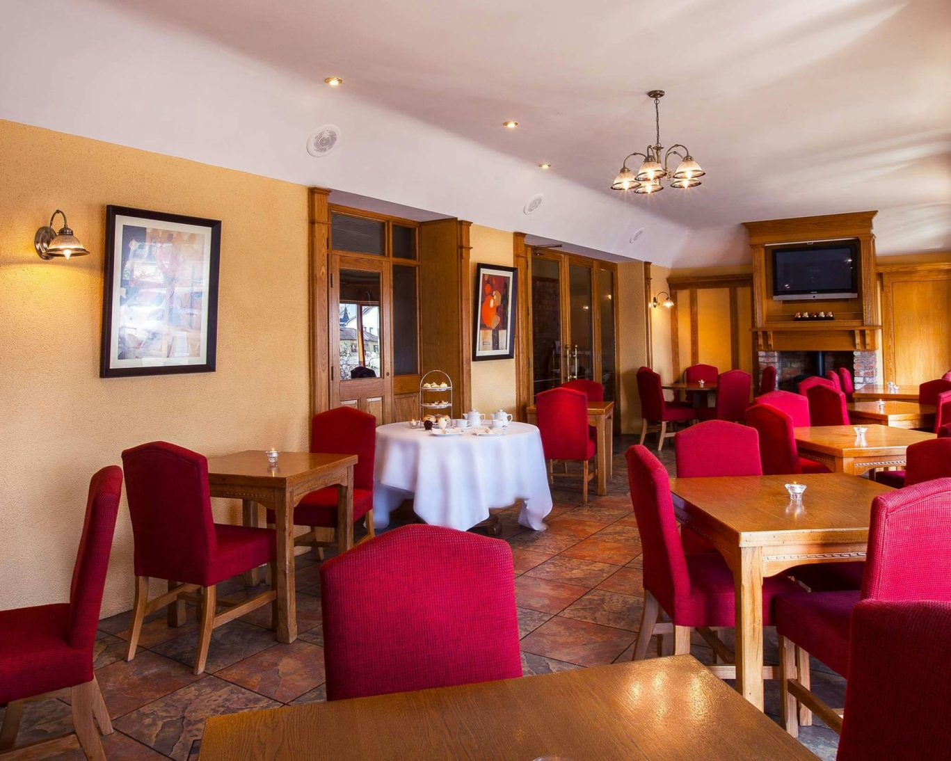Bright dining area at The Castle Arch Hotel with wooden tables and red upholstered chairs.