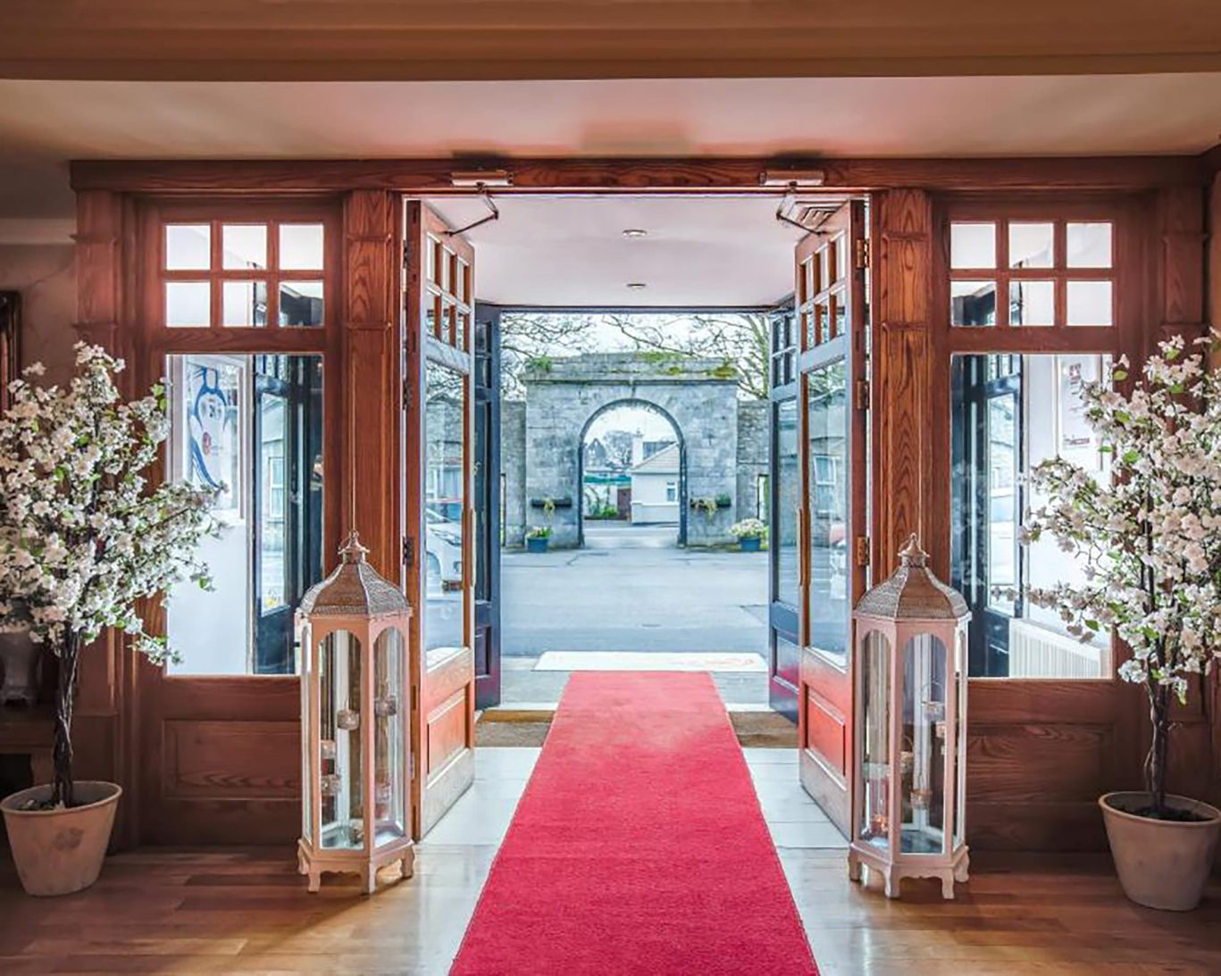 Red carpet entrance inside The Castle Arch Hotel looking out through wooden double doors and stone gateway.