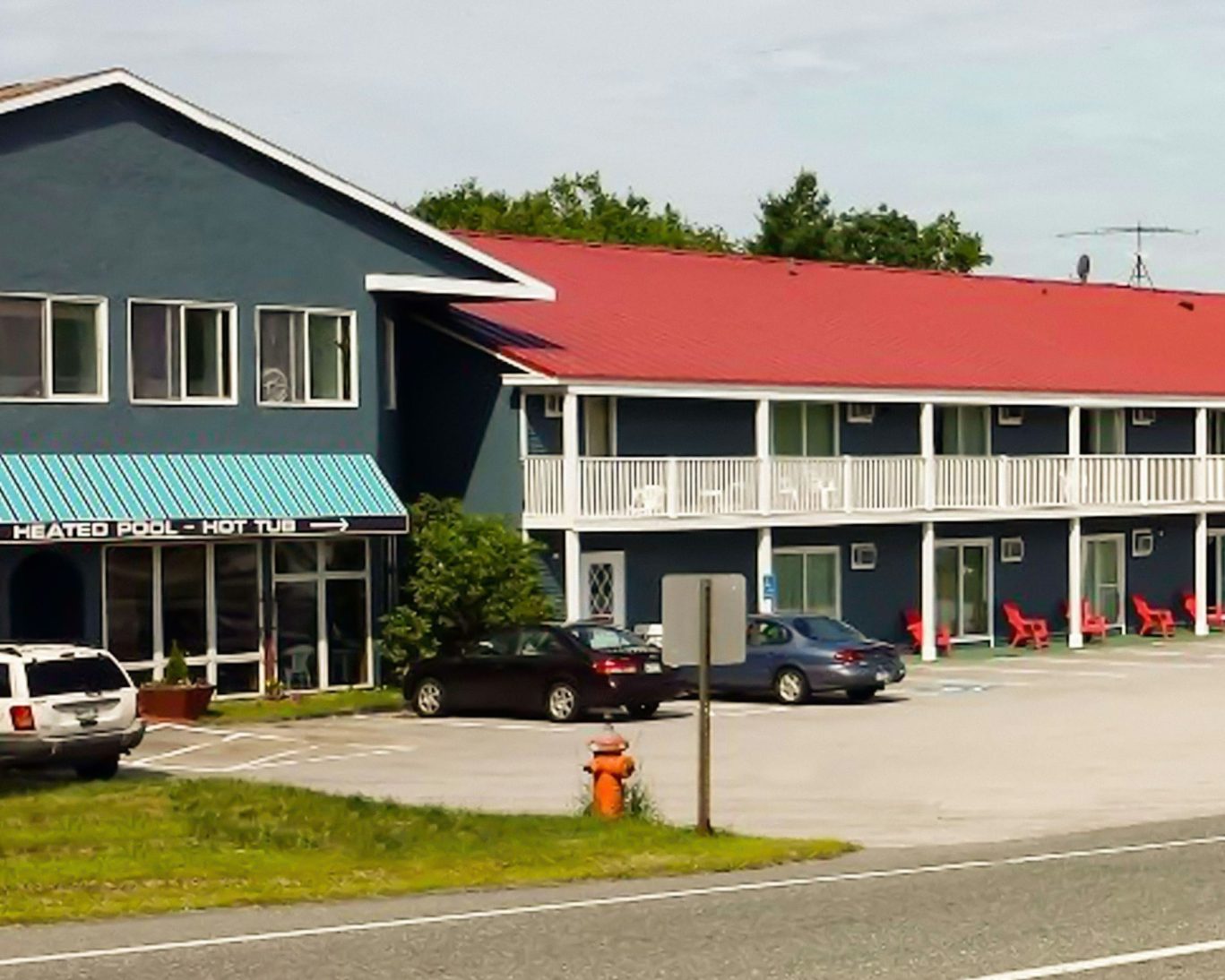 Exterior view of Colonial Motel with red roof, blue siding, guest parking, and balcony seating.