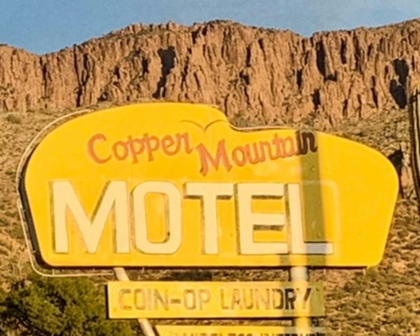 Vintage Copper Mountain Motel sign with mountain backdrop in Arizona desert.