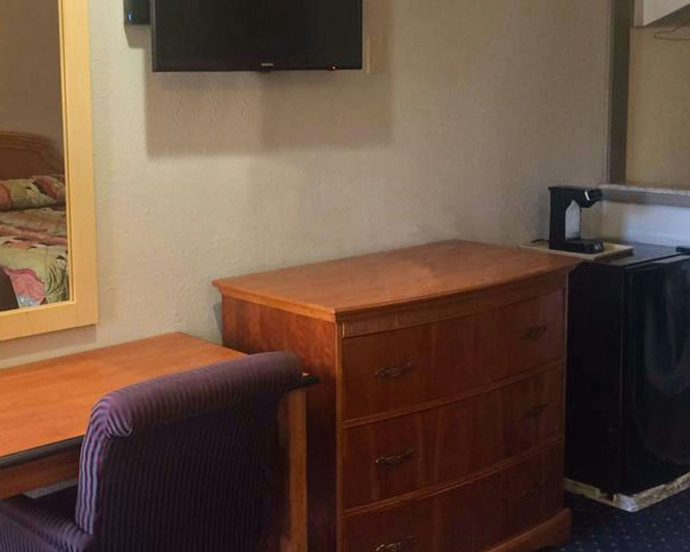 Guest room interior at Crown Lodge Motel with TV, dresser, work desk, and mini fridge.