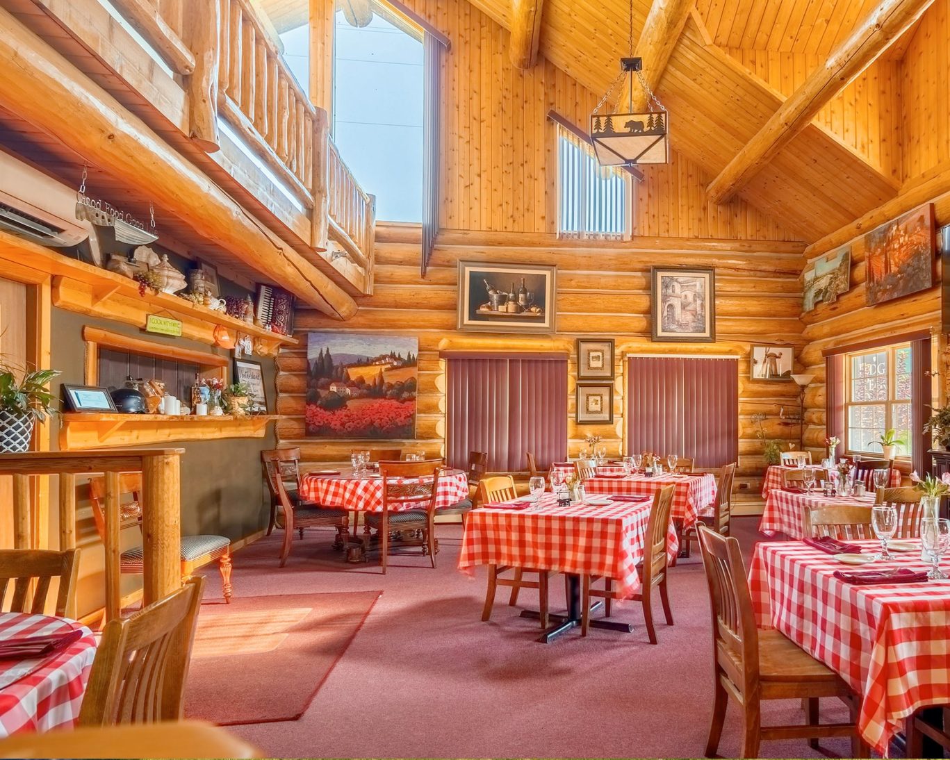 Rustic dining area inside Dodge Peak Lodge with log walls and red checkered tablecloths.