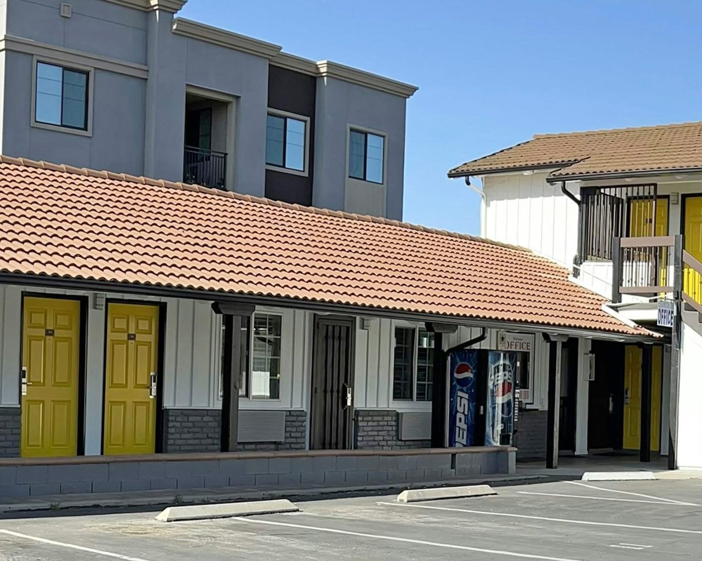 Exterior of Escondida Motel with vibrant yellow doors, tiled roof, and guest parking area.