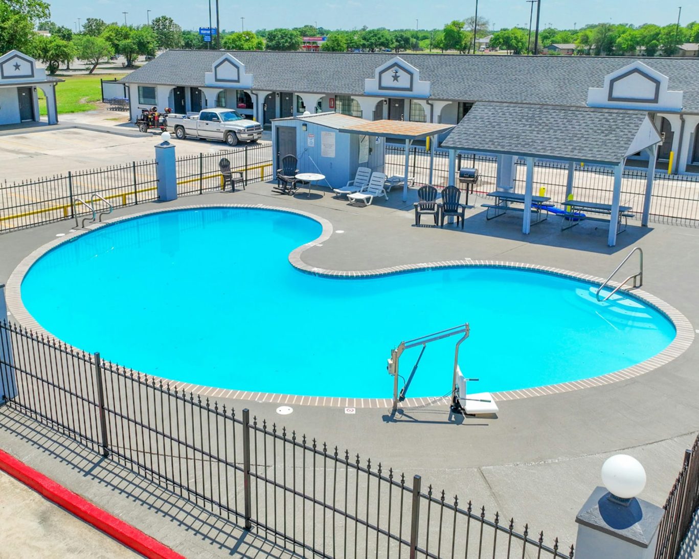 Hondo Executive Inn outdoor pool area with seating, shaded pavilion, and secure gated access.