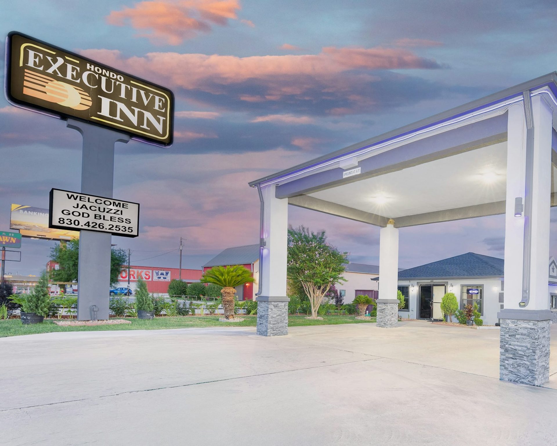 Hondo Executive Inn welcoming front canopy and illuminated sign at sunset with a view of nearby attractions.