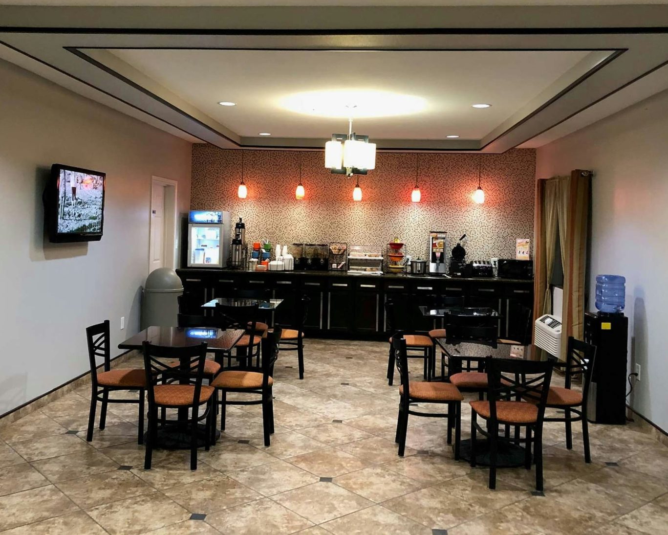 Complimentary breakfast area at Executive Inn & Suites with dining tables, cereal bar, and coffee station.