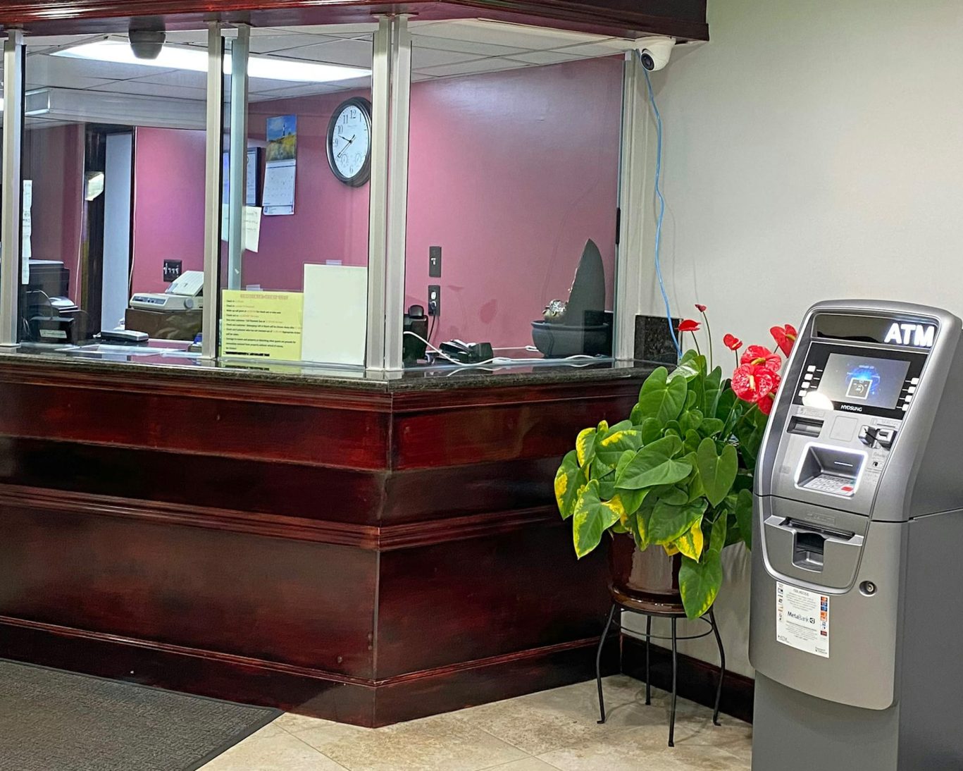 Secure hotel front desk with glass partition, dark wood trim, and on-site ATM at Express Inn Newport.