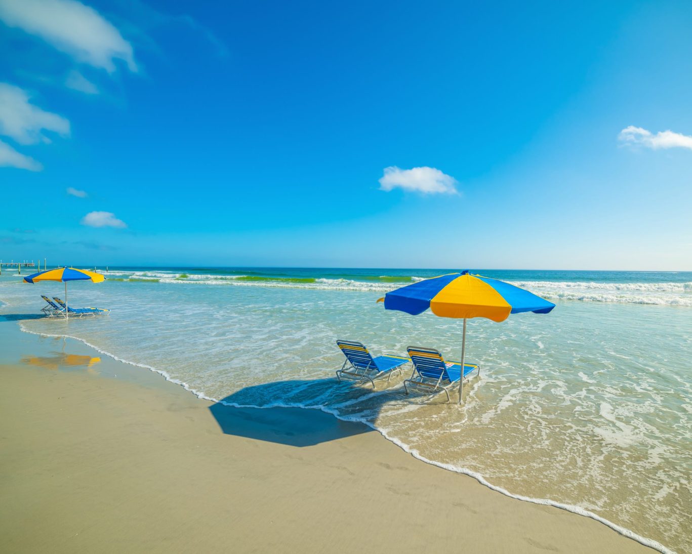 Sunny Daytona Beach shoreline with beach chairs and umbrellas near Fountain Beach Resort oceanfront location.