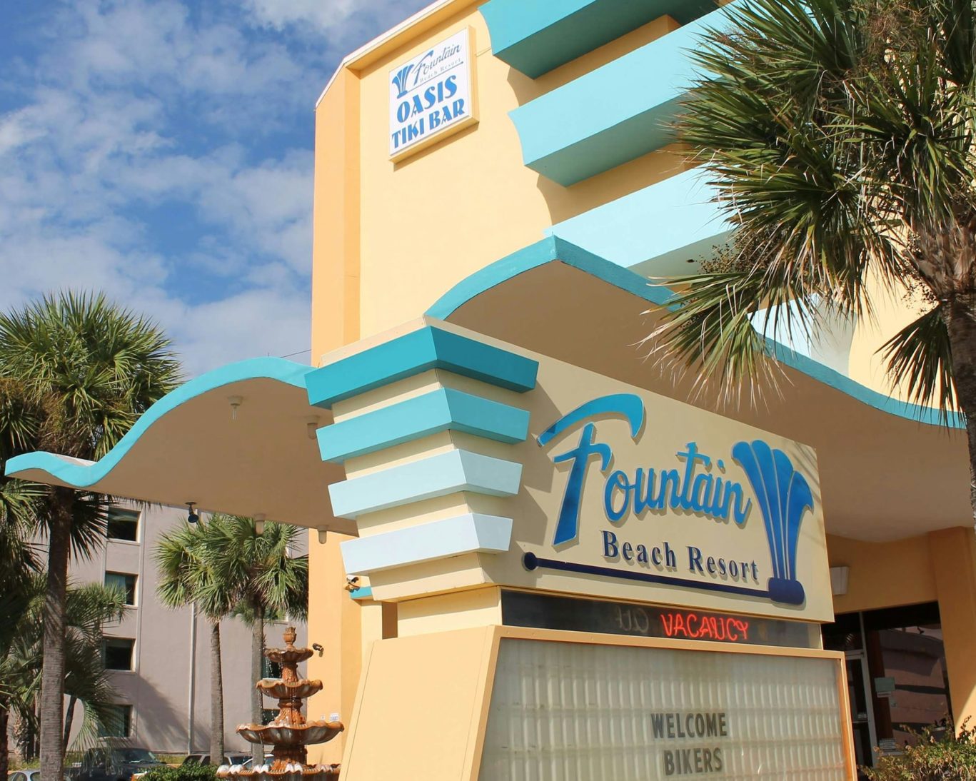 Fountain Beach Resort exterior with colorful retro signage and palm trees near Daytona Beach shoreline.