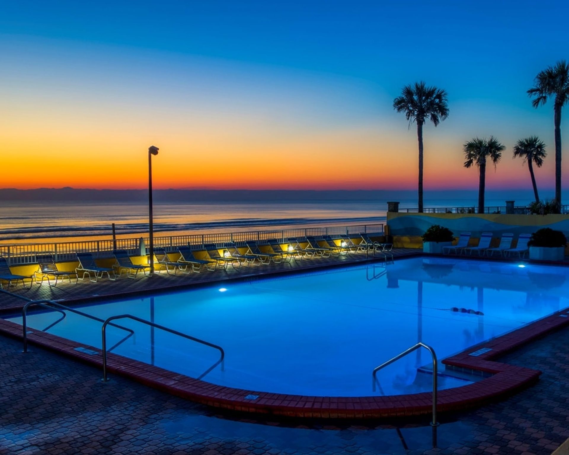 Oceanfront swimming pool at Fountain Beach Resort with sunrise views, palm trees, and ample poolside lounge chairs.