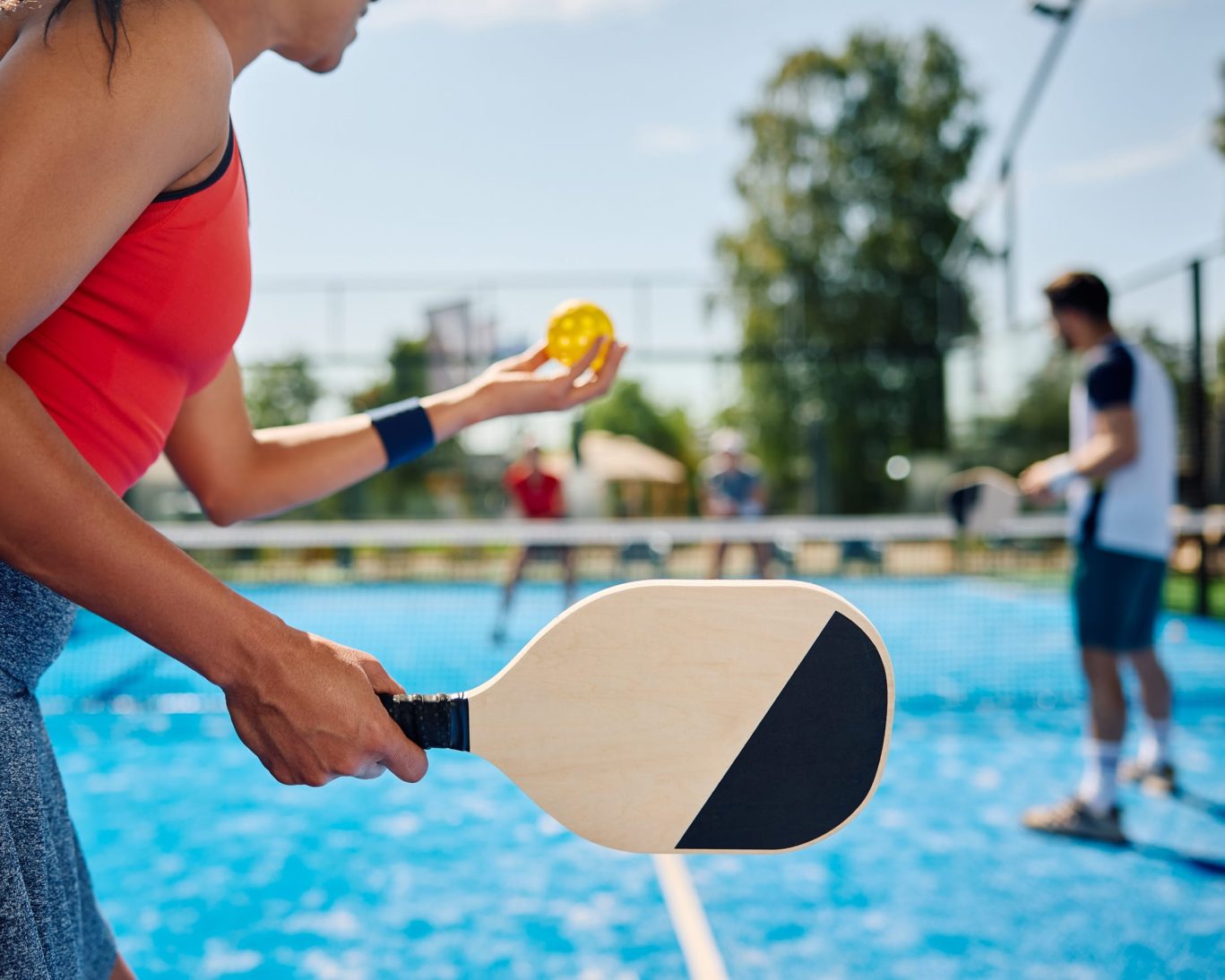 Woman holding pickleball paddle and ball on outdoor court at Tower Park during a sunny game.