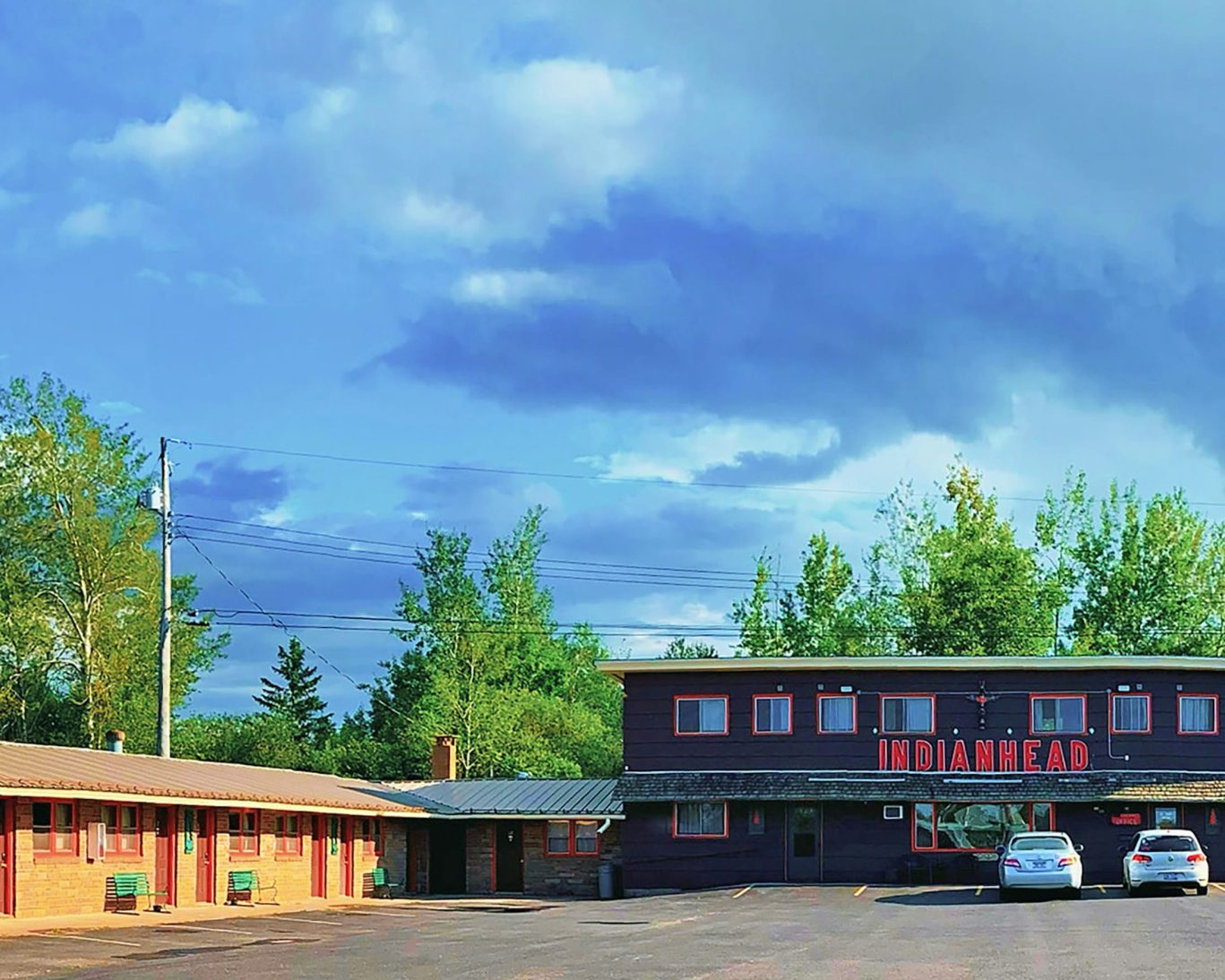 Front exterior of Indianhead Motel surrounded by trees with parking area and guest rooms.