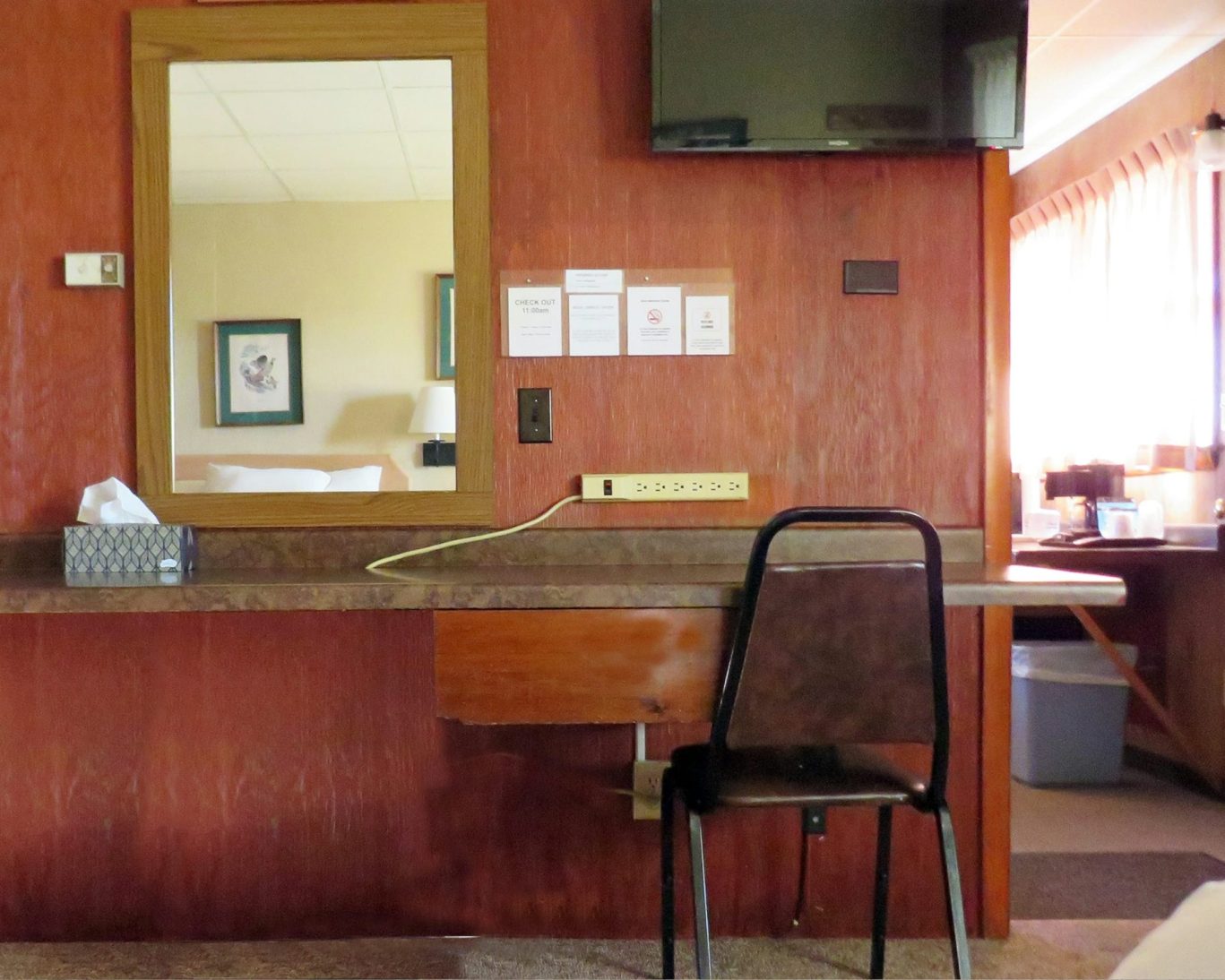 Guest room desk setup at Indianhead Motel with mirror, chair, flat-screen TV, and power strip.