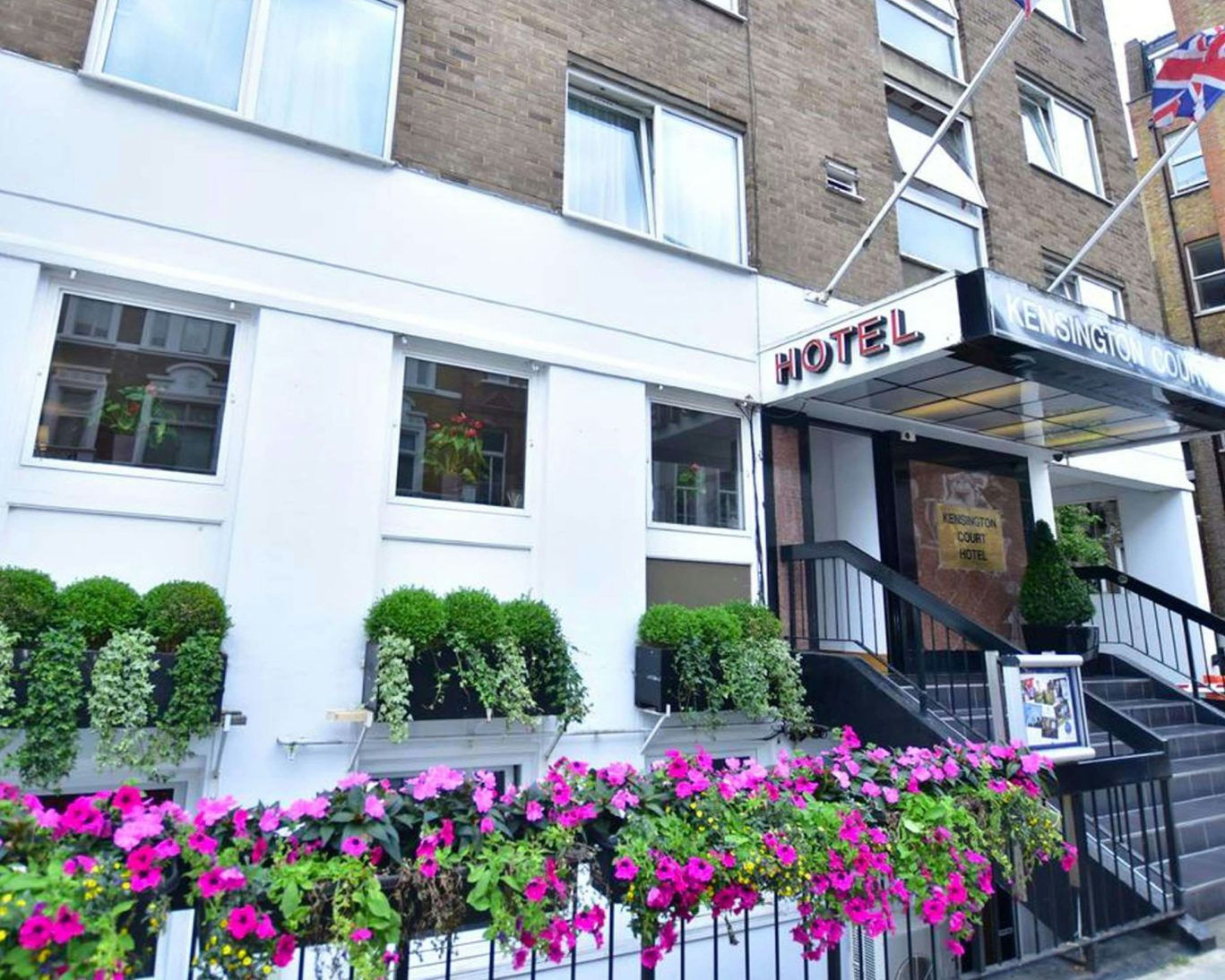 Exterior view of Kensington Court Hotel in London with floral decoration.s and Union Jack flags