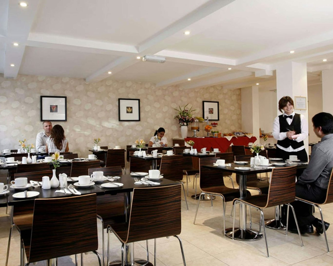 Guests dining in the breakfast room at Kensington Court Hotel with buffet and modern decor.