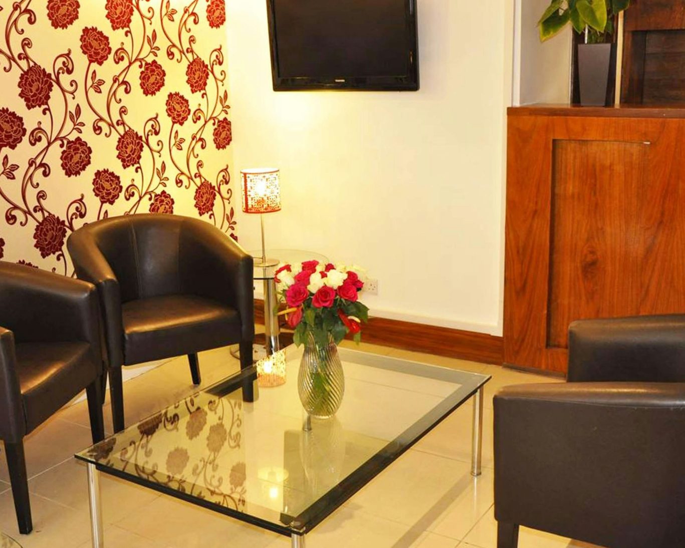 Lobby seating area at Kensington Court Hotel featuring leather chairs, floral decor, and flat-screen TV.