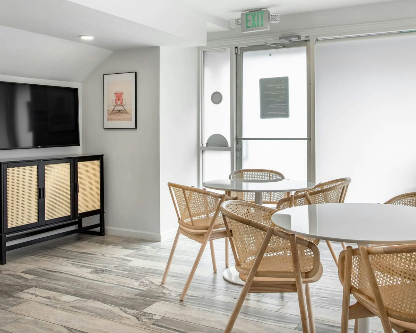 Bright motel breakfast area with TV, round tables, and rattan chairs.