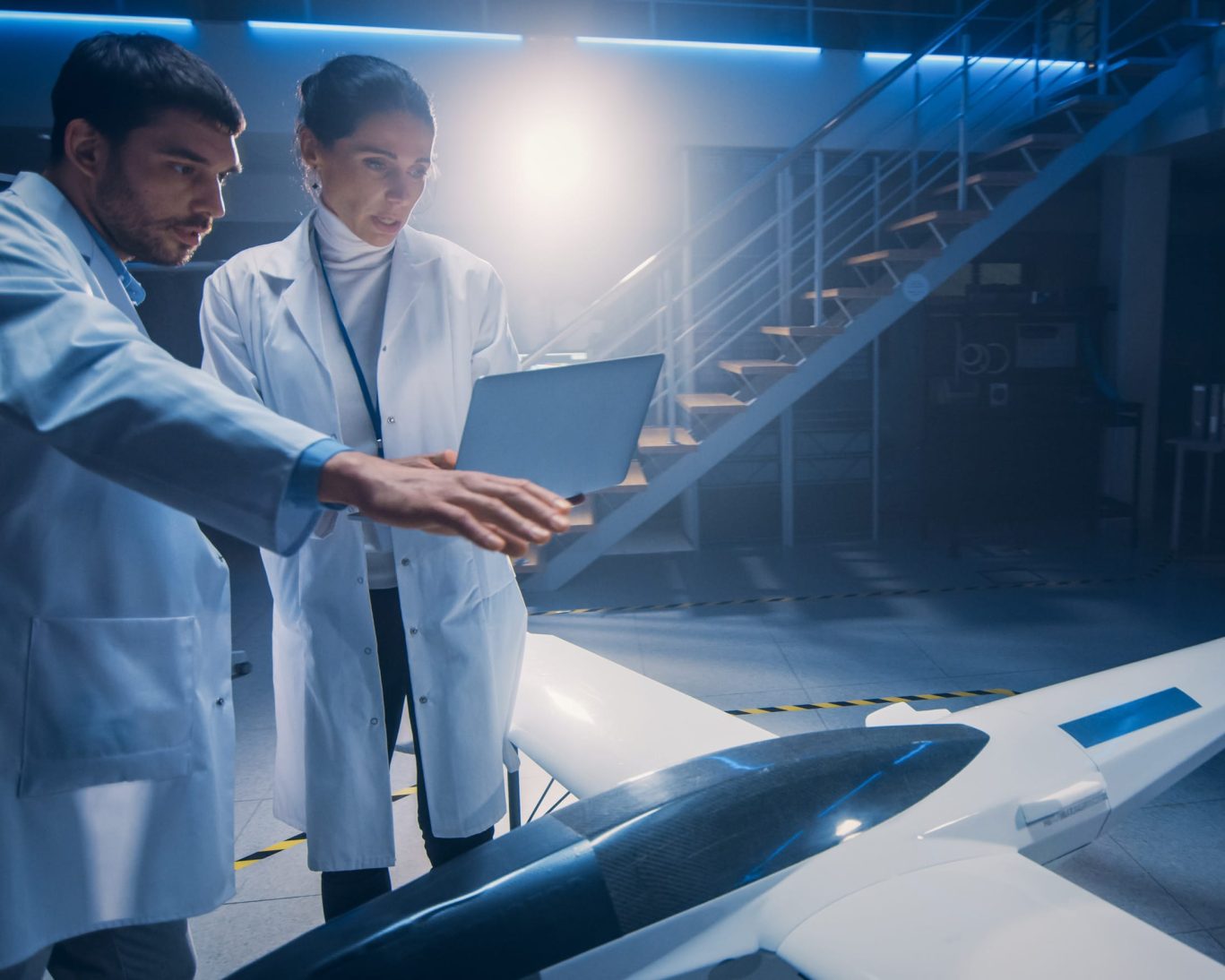 Two aerospace engineers in lab coats working on an unmanned aircraft prototype in a high-tech research lab.