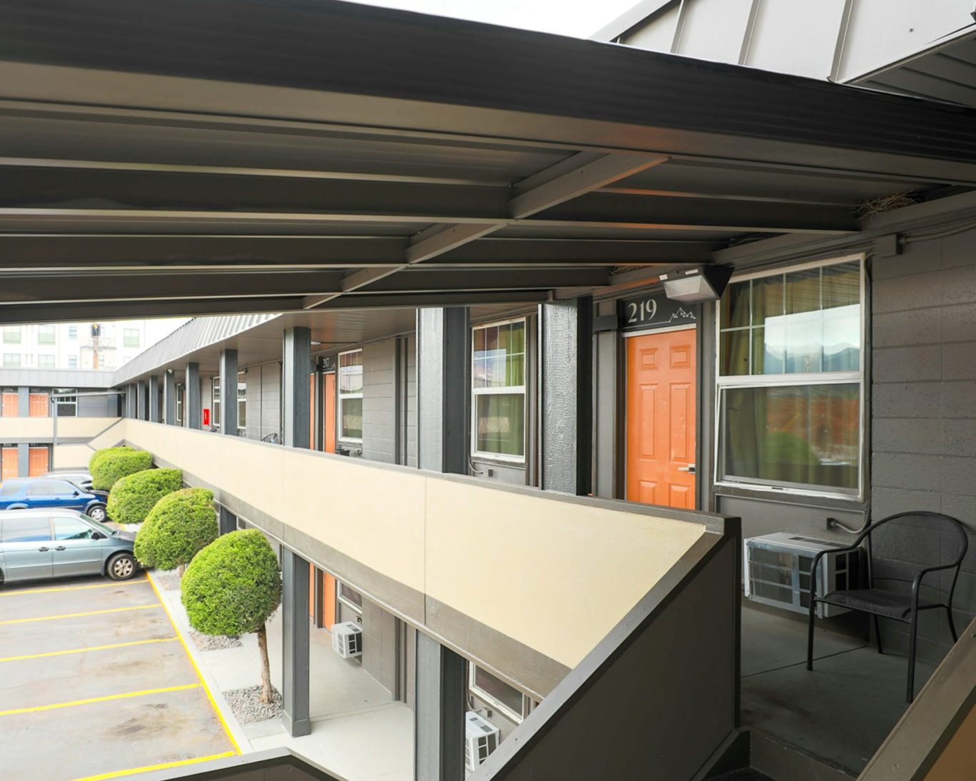 Second-story walkway and exterior of Modern Motel with orange doors and parking.