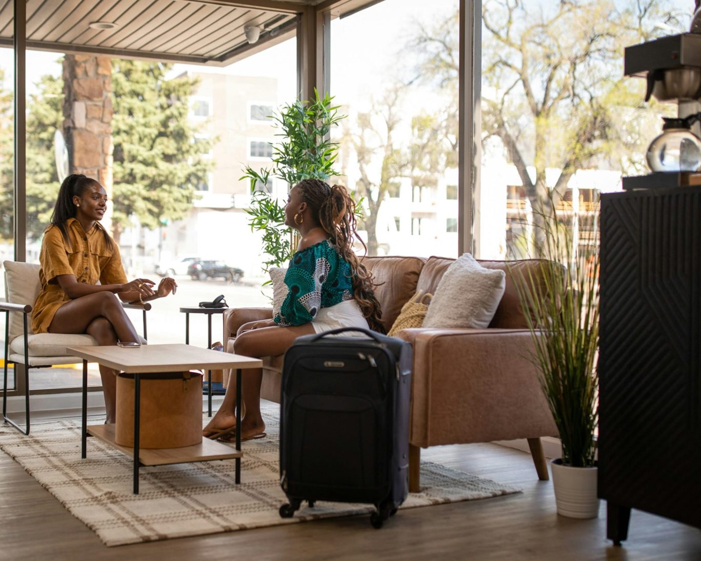 Guests relaxing in Modern Motel lobby with luggage and large windows.
