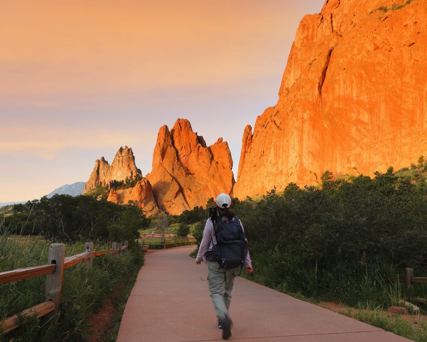 Hiker walking along scenic trail at Garden of the Gods with towering red rock formations at sunrise in Colorado Springs.