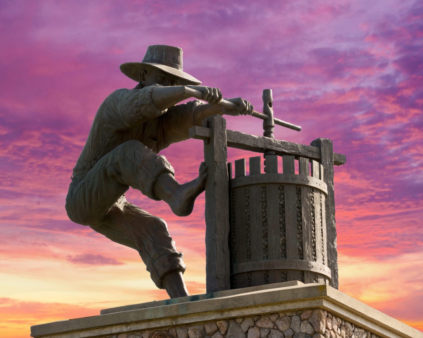 Iconic Grape Crusher statue in Napa Valley silhouetted against a vibrant sunset sky.