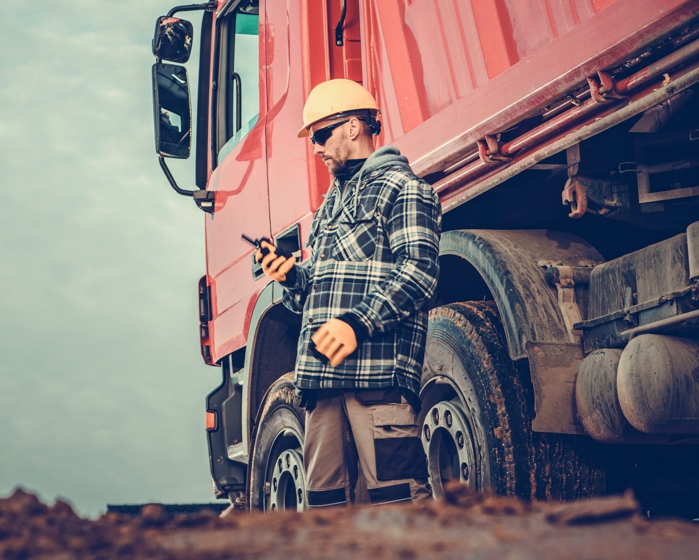 Construction or logistics worker in safety gear standing beside a red semi-truck at Rugby Manufacturing near Northern Lights Inn.