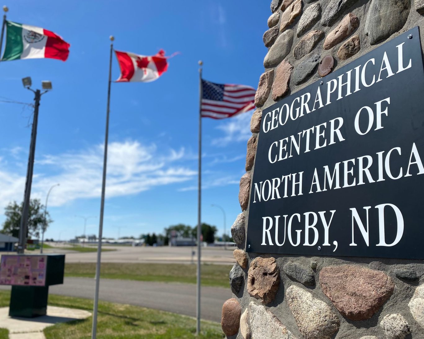 Monument marking the Geographical Center of North America in Rugby, ND, with flags of Mexico, Canada, and the U.S. in the background.