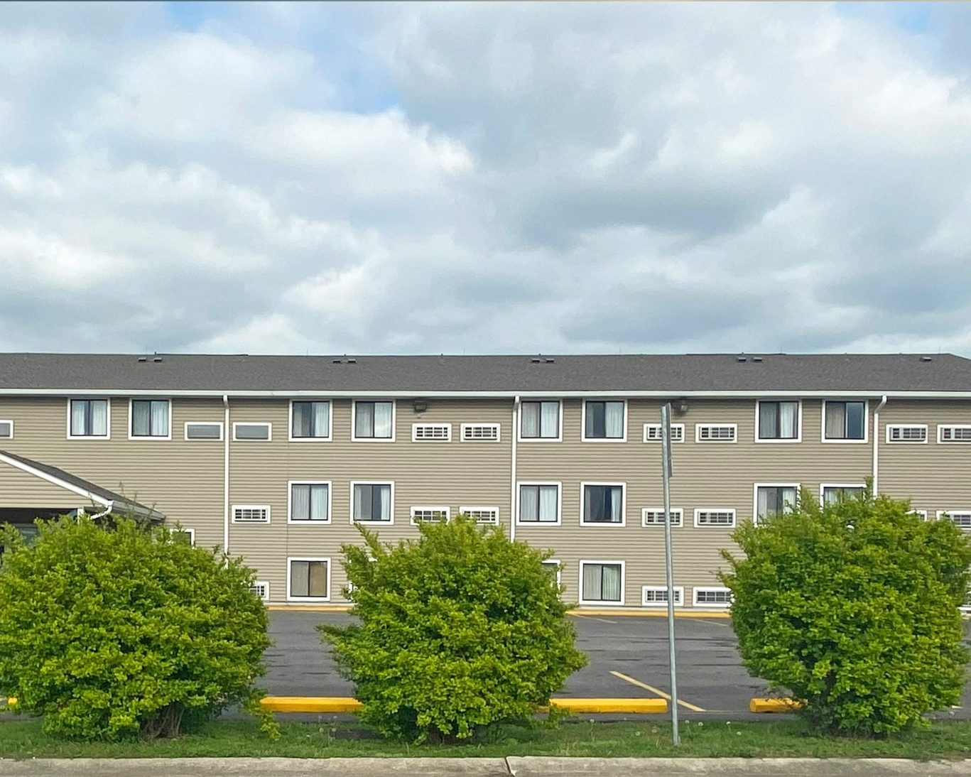 Three-story exterior of Oak Grove Inn with ample parking and landscaped shrubs under a cloudy sky.