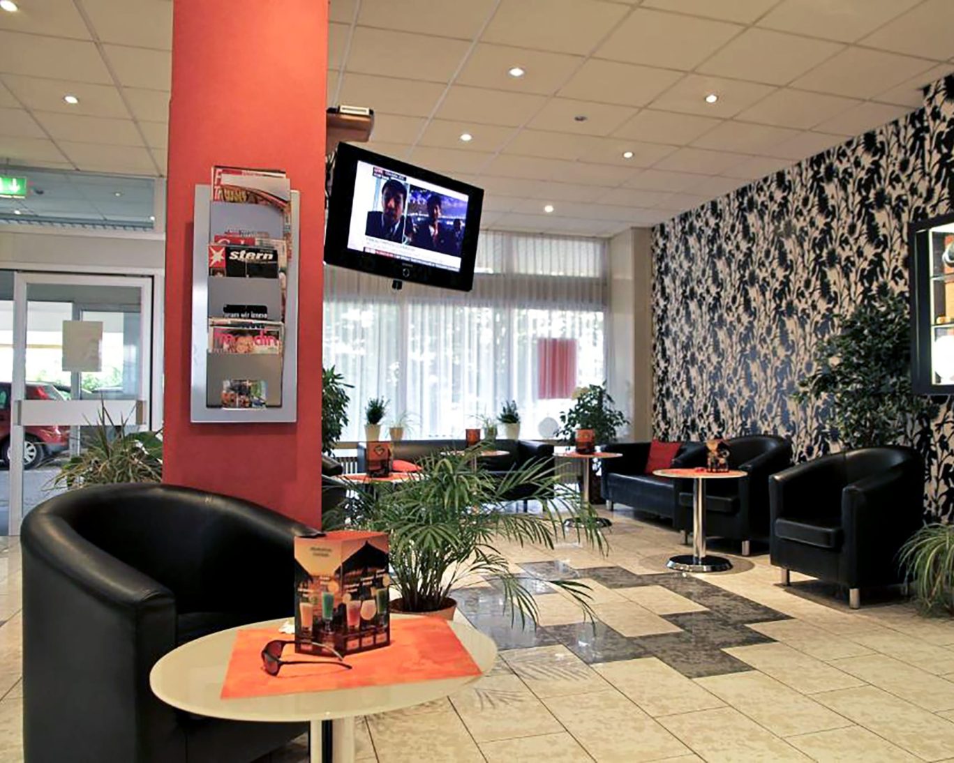 Modern Opal Hotel lounge area with black leather chairs, flat-screen TV, and patterned wallpaper.