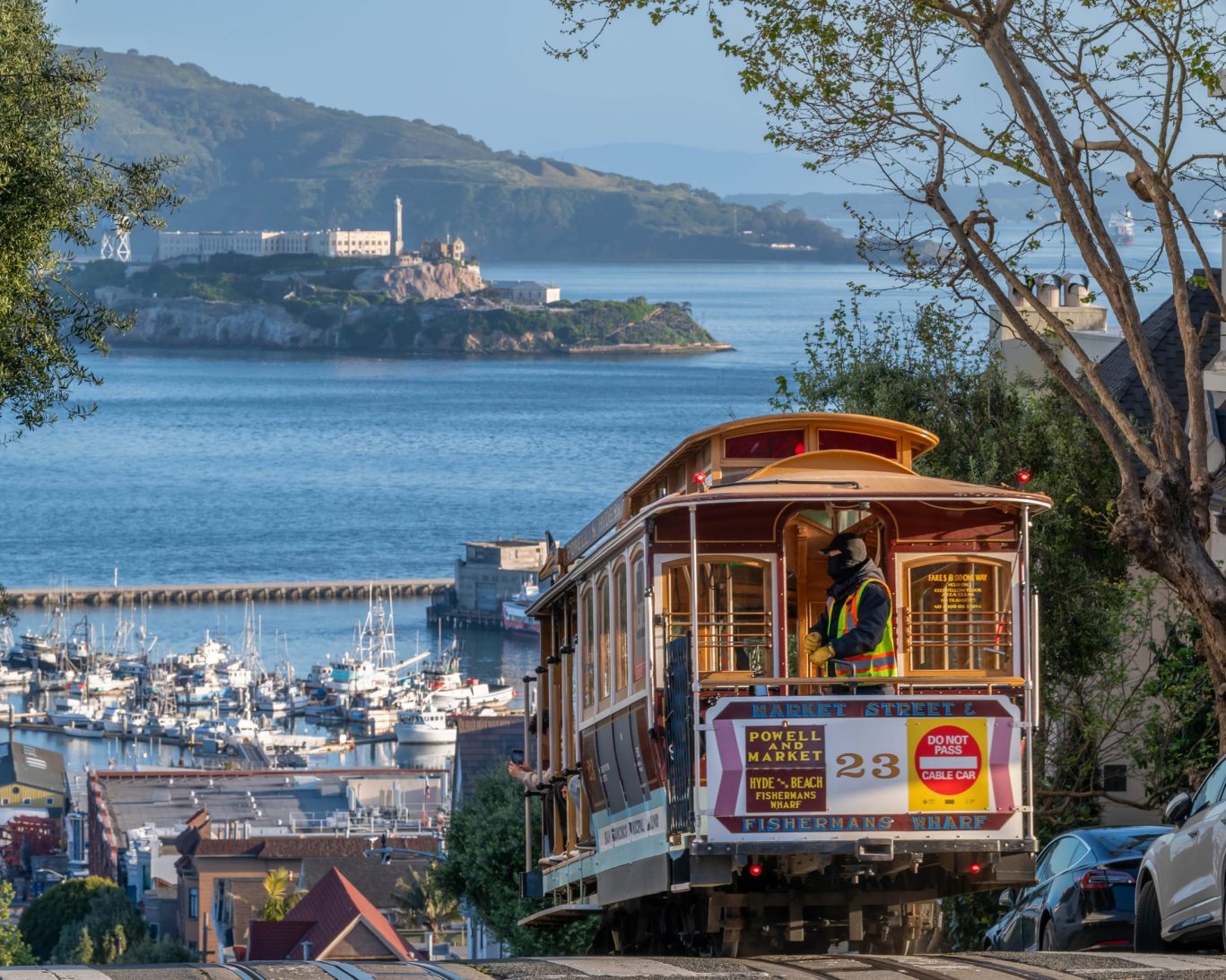 Historic cable car climbing a hill in San Francisco with Alcatraz Island and marina in the background.