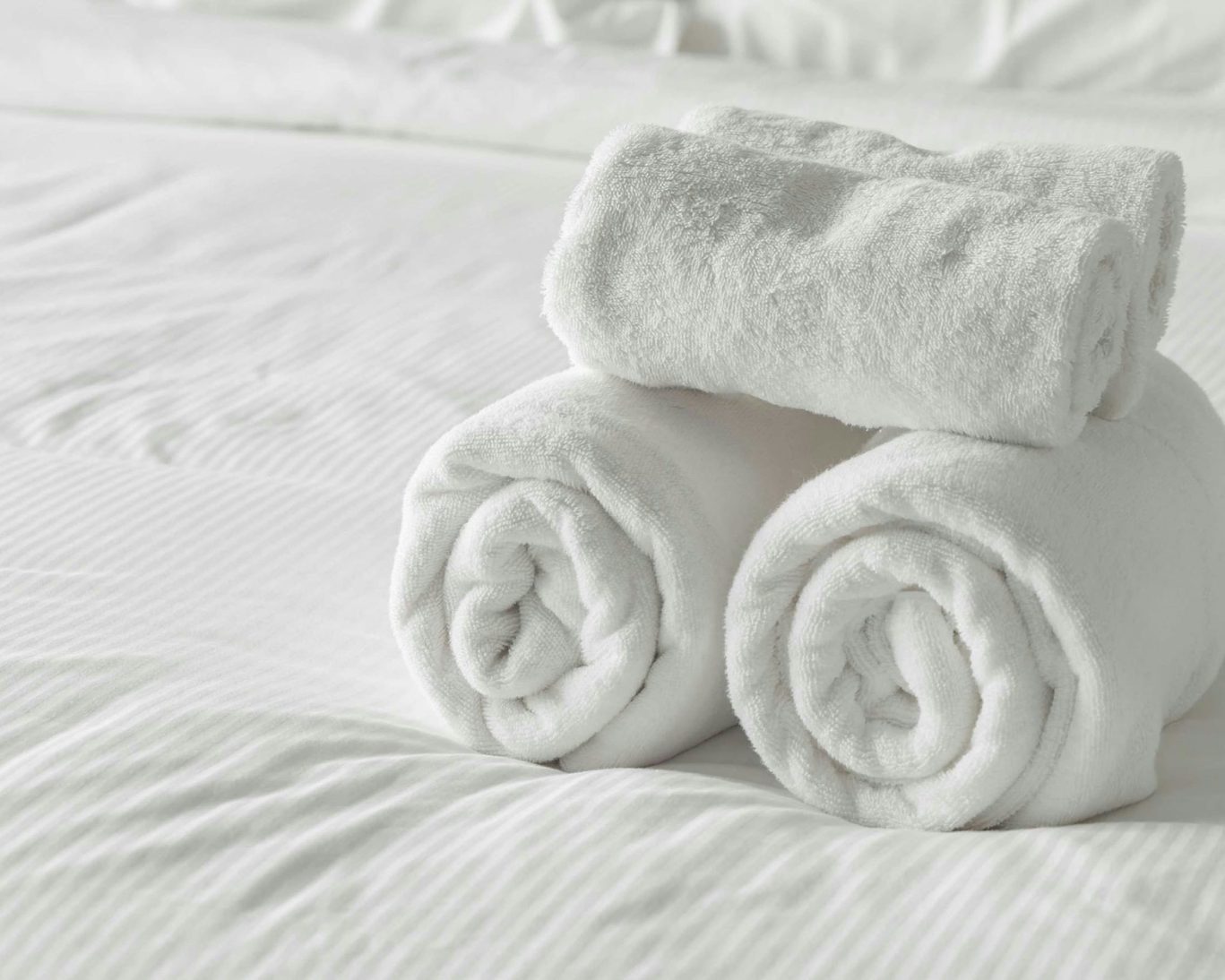 Rolled fresh white towels placed on a neatly made bed at Rama Inn Bells.