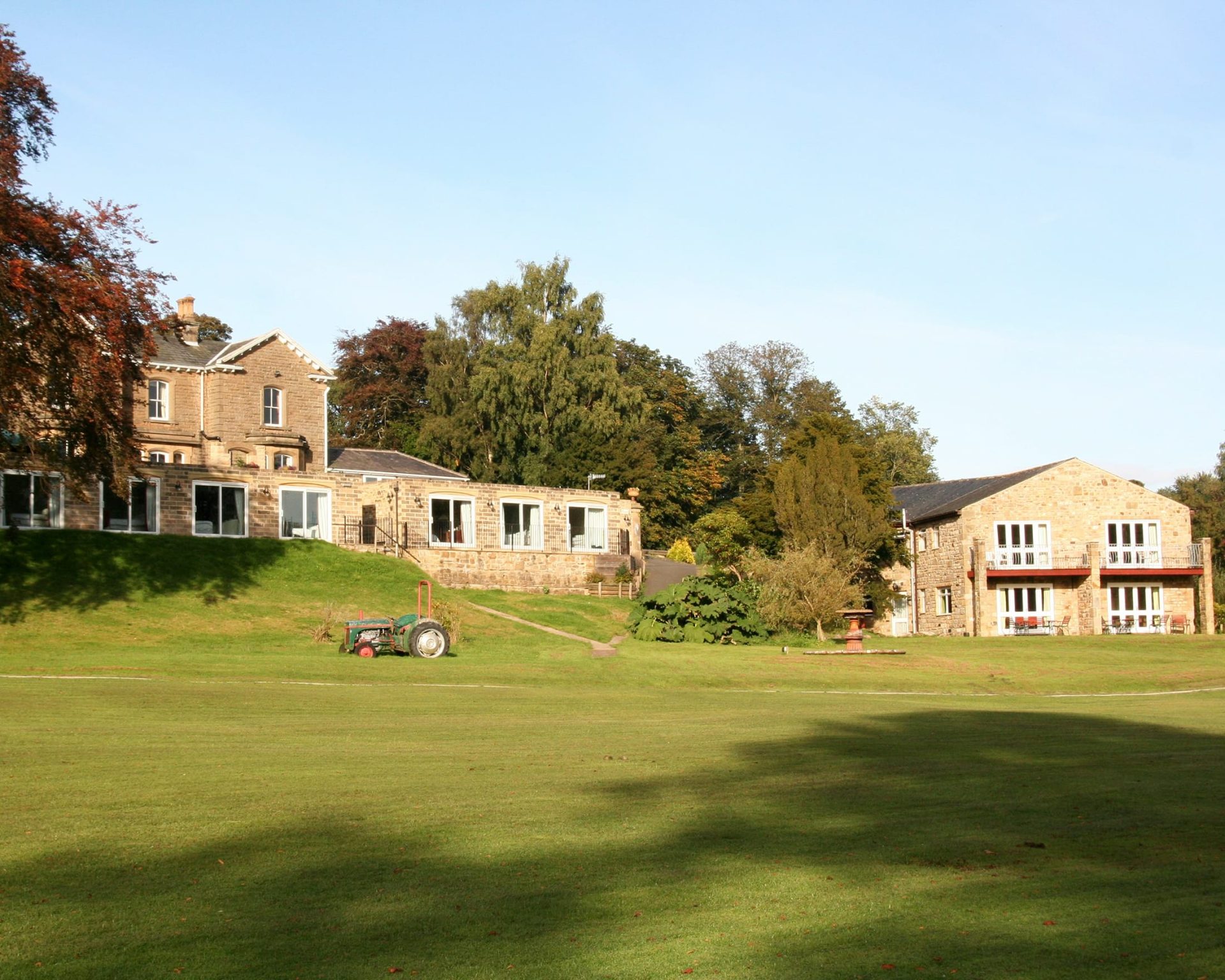 Riverdale Hall Hotel buildings surrounded by green lawn and trees on a sunny day.