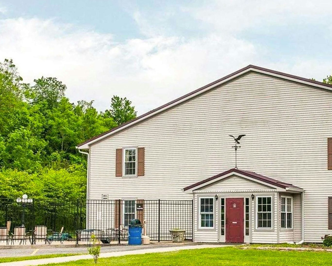 Front exterior of Royal Inn Rockville with red door entrance and fenced outdoor seating area surrounded by trees.