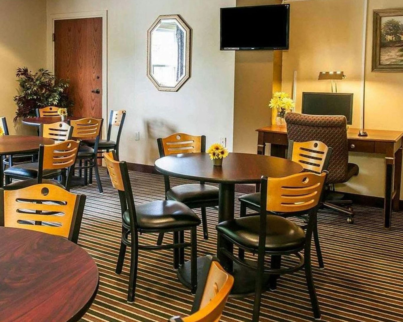 Casual breakfast area at Royal Inn Rockville featuring round tables, yellow chairs, and a guest-use computer workstation.