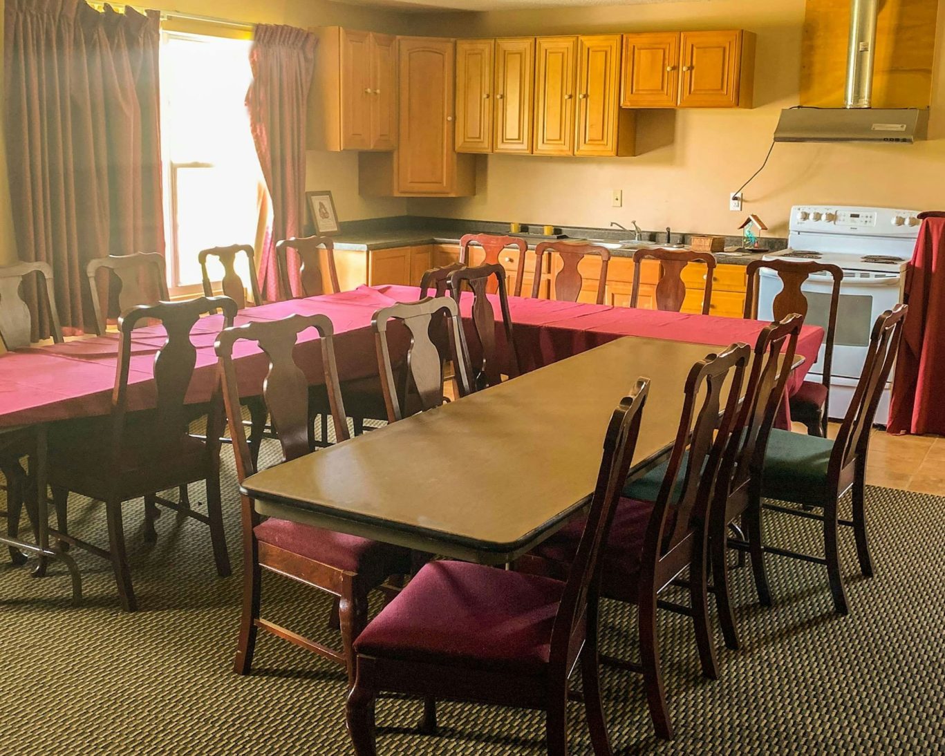 Multi-purpose meeting and dining space at Royal Inn Rockville with long tables, wooden chairs, and a fully equipped kitchen.