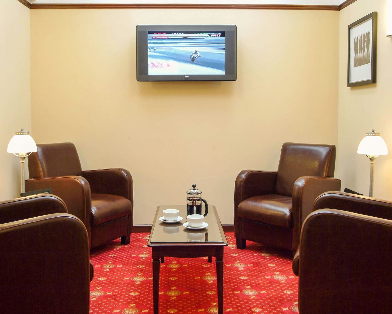 Cozy leather armchairs in guest lounge at The Hollies Hotel with flat-screen TV and red carpet.