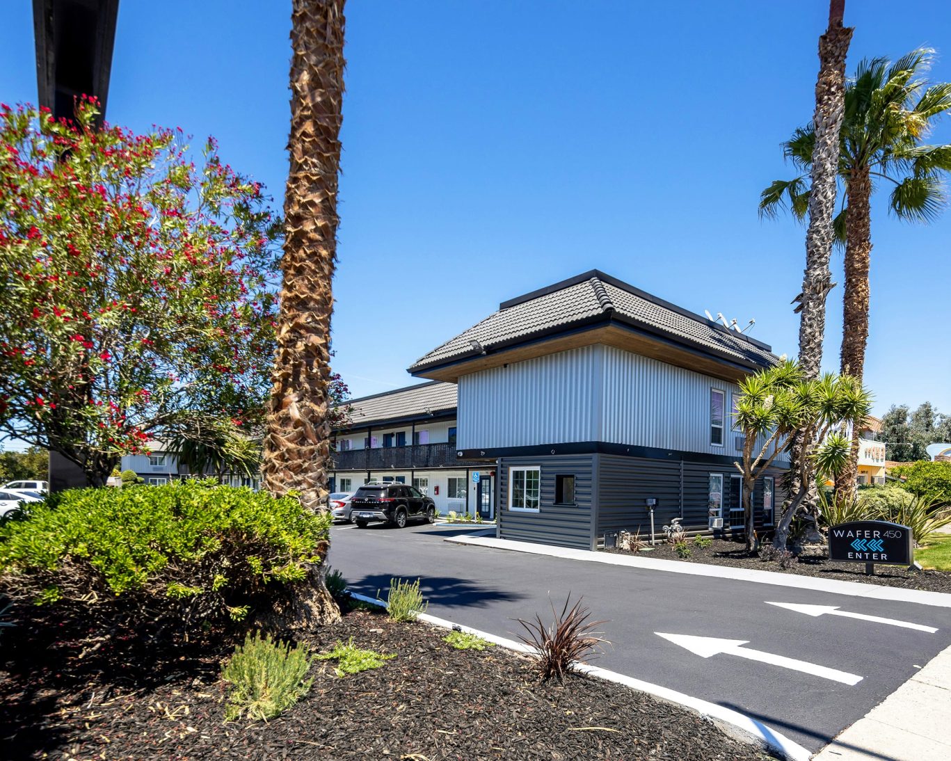 Modern exterior of Wafer 450 Hotel with palm trees, driveway, and guest parking in San Jose.