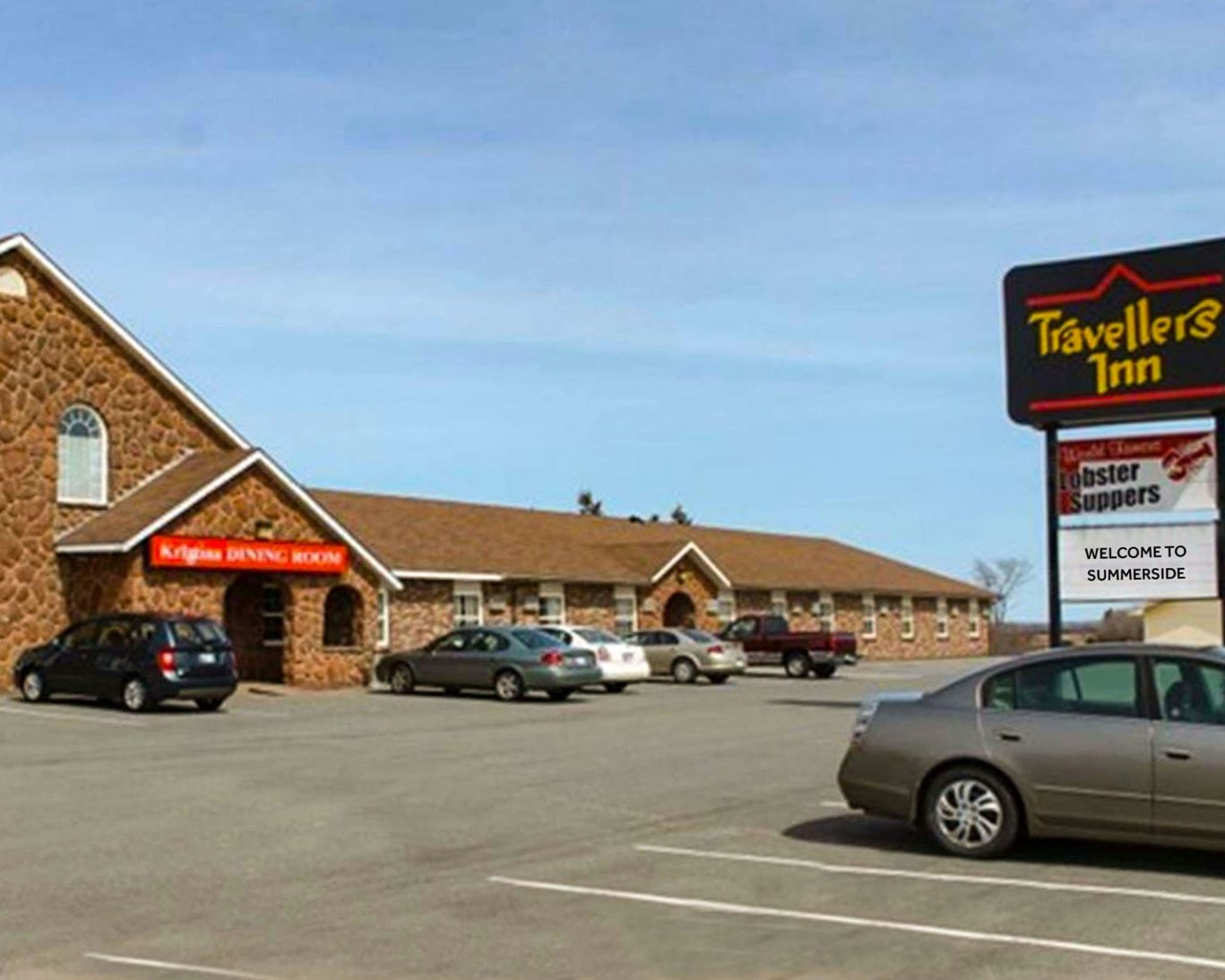 Exterior of Travellers Inn Summerside with large parking lot and on-site dining at Krigina’s Dining Room.