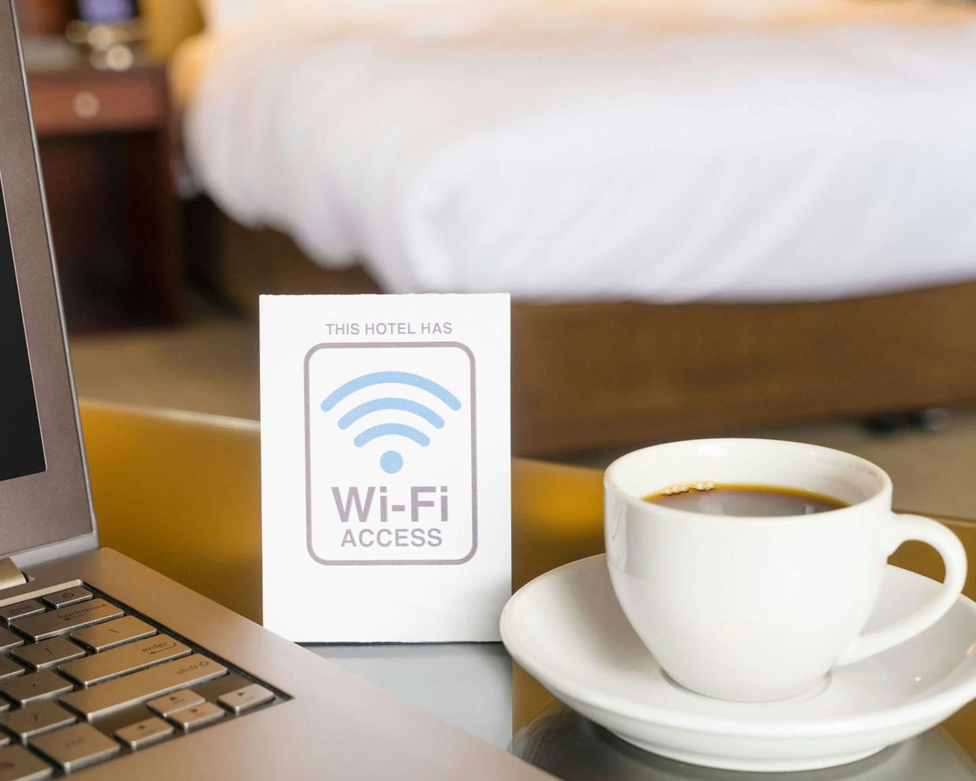 Hotel room workspace with coffee cup, laptop, and Wi-Fi sign on table.