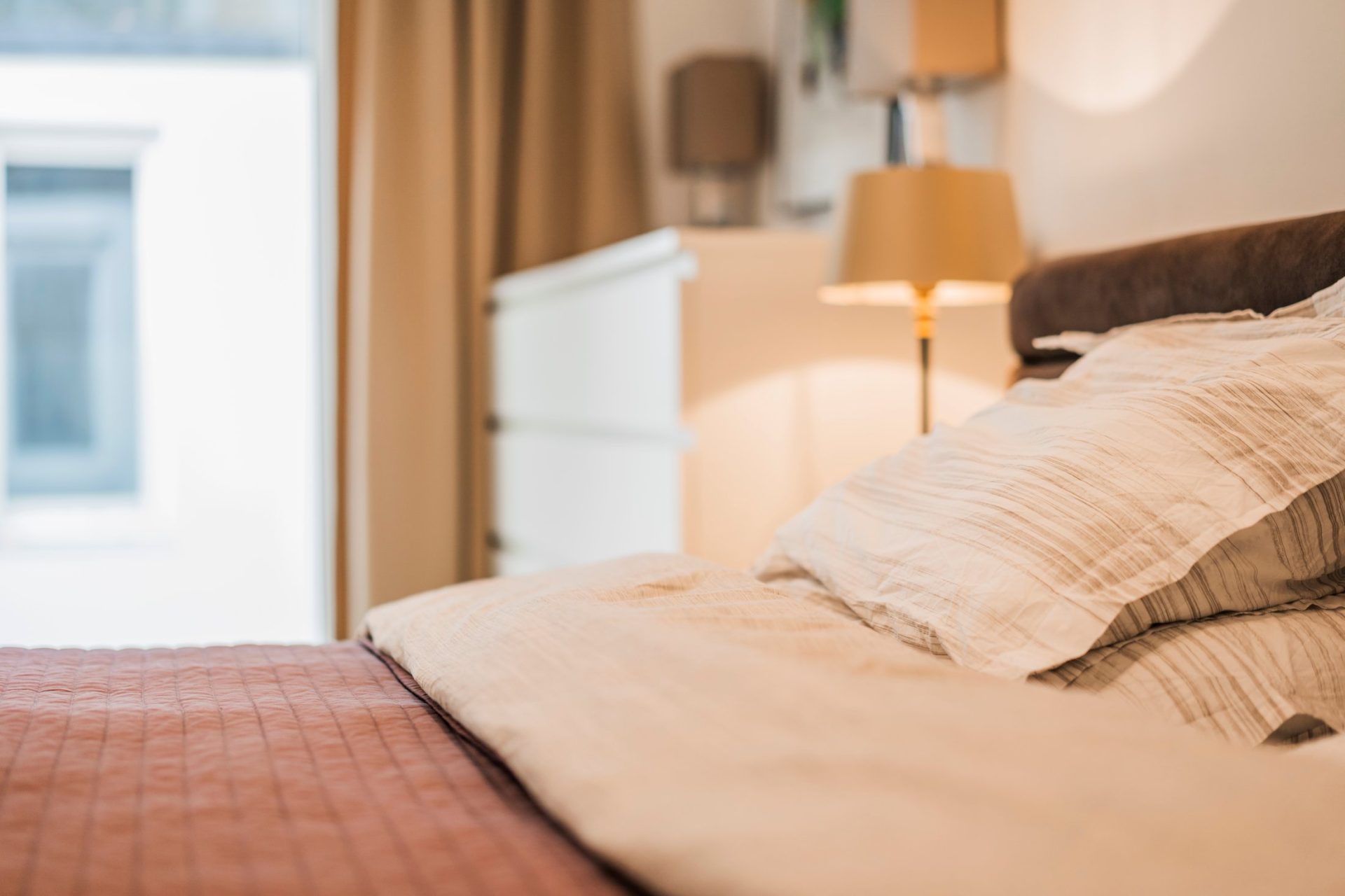 Close-up of cozy, neatly made bed with soft lighting in stylish hotel room.