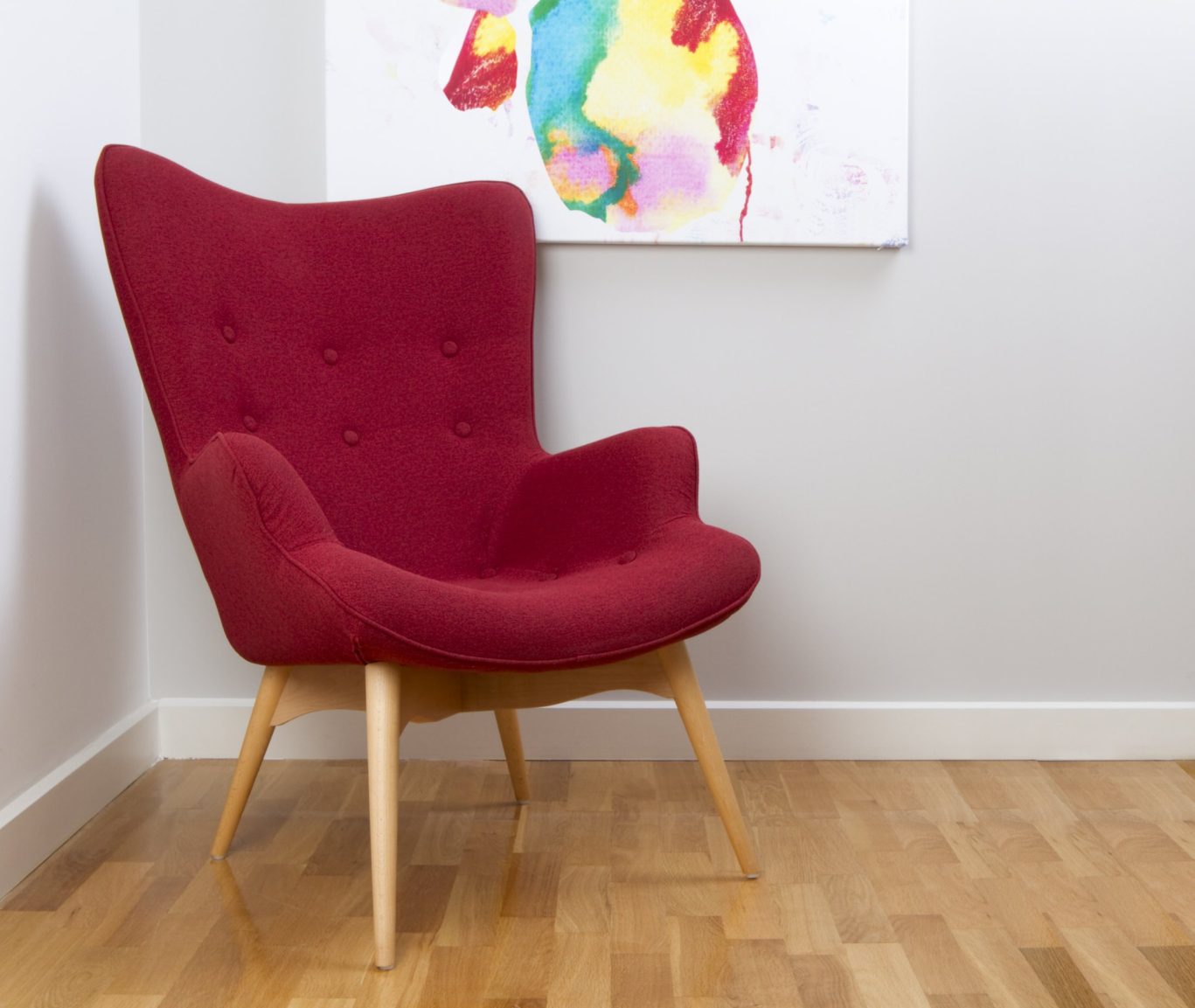 Mid-century modern red accent chair with colorful abstract wall art.
