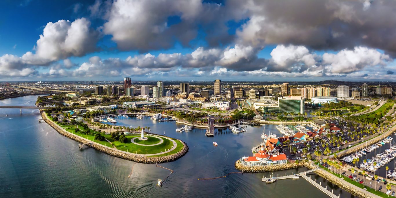 Scenic aerial view of Long Beach marina and skyline with boats, green spaces, and dramatic clouds.