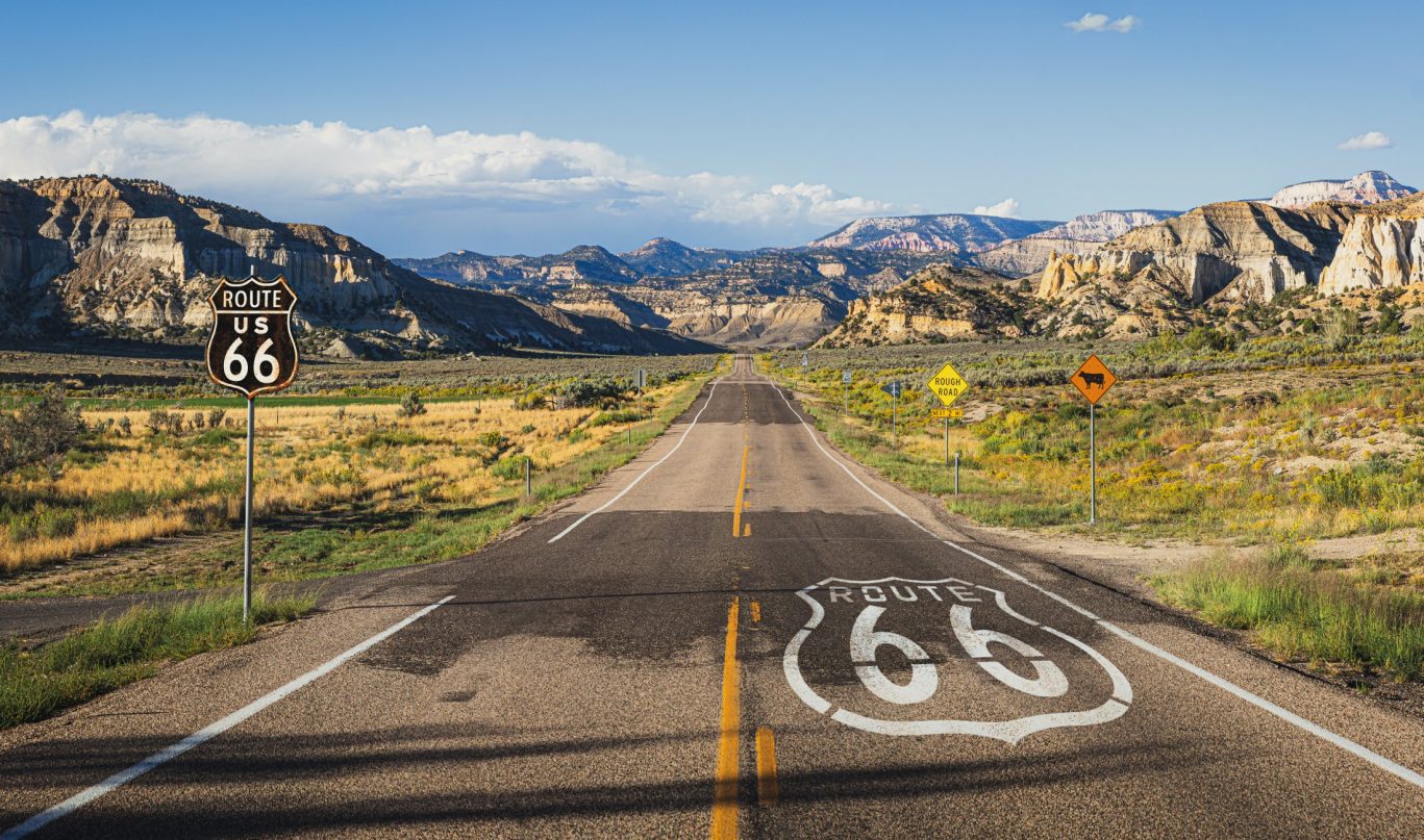 Iconic Route 66 road stretching into the distance through scenic Utah desert with rock formations.