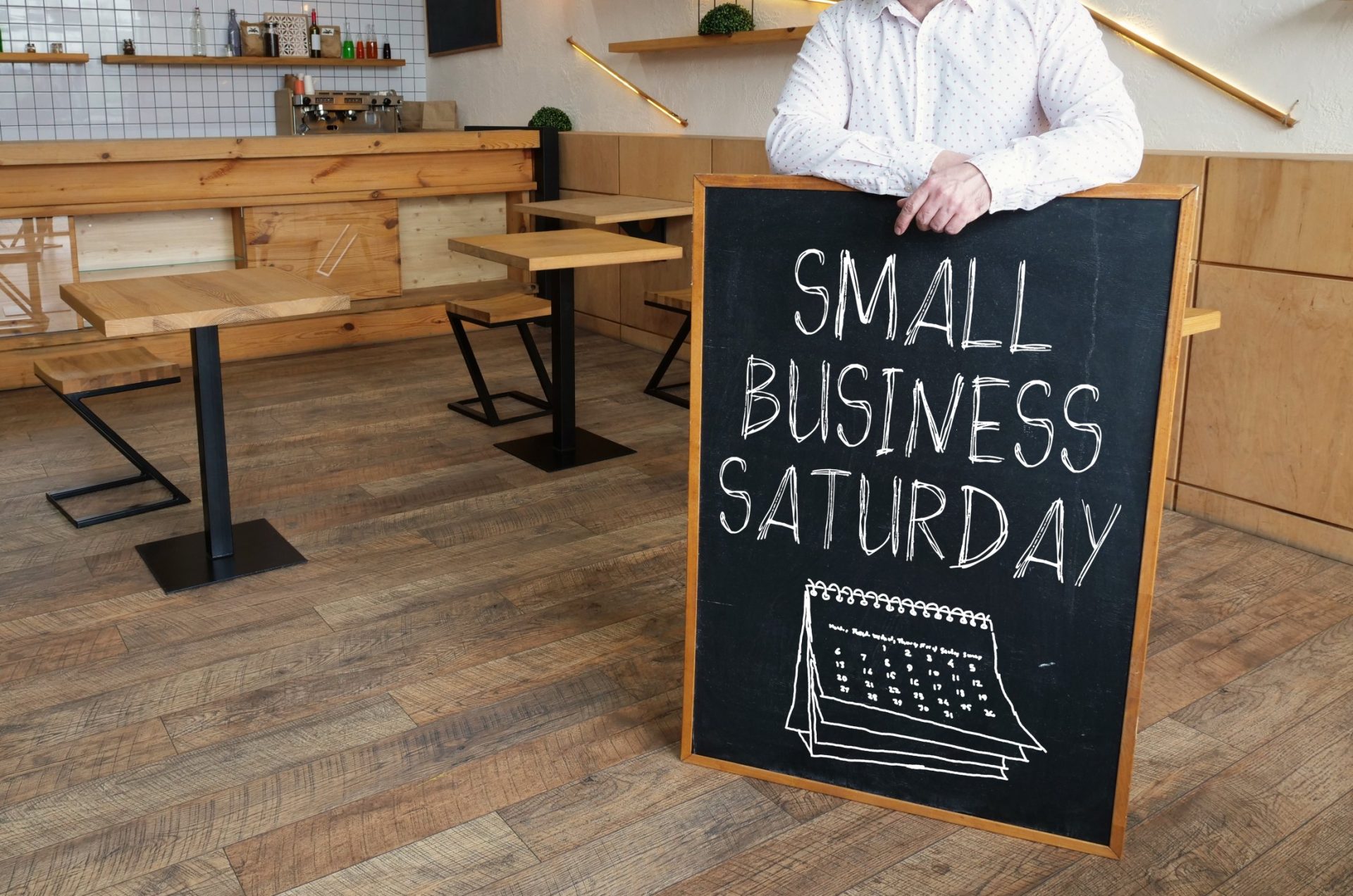 Small business owner promoting Small Business Saturday with chalkboard sign in local café.